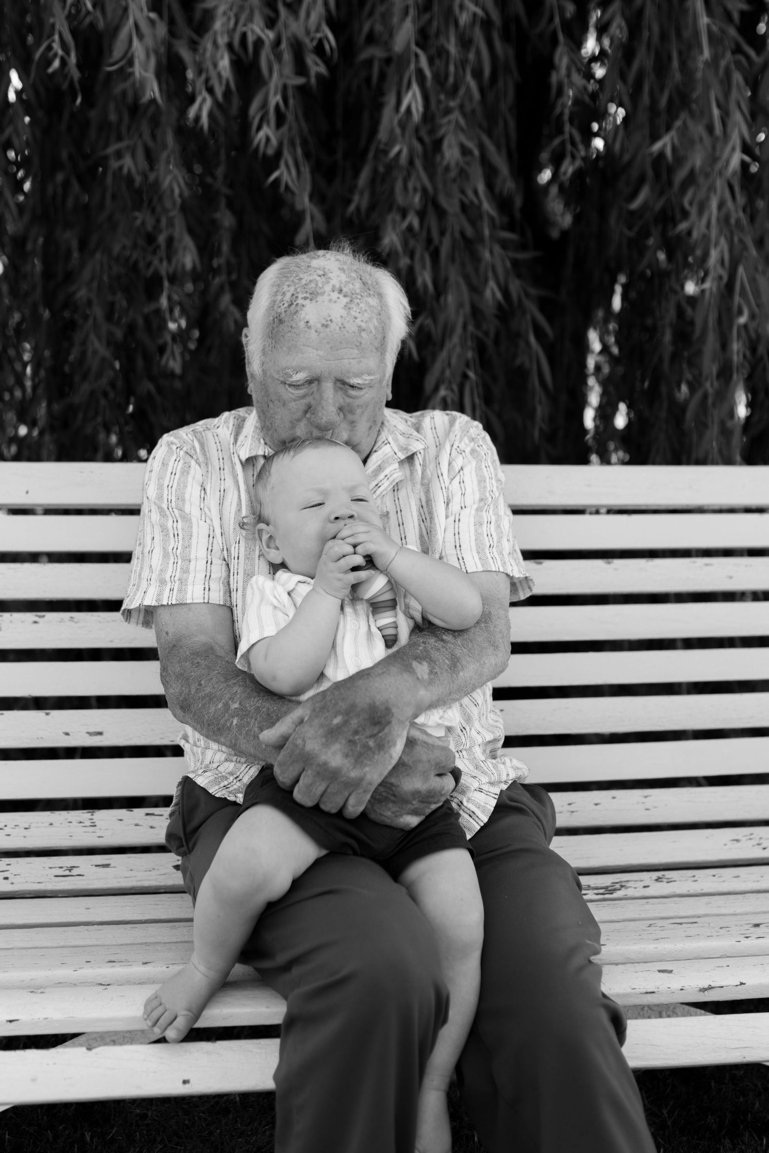 A person sits on a white park bench in a black and white photo series showing them drinking from a bottle.