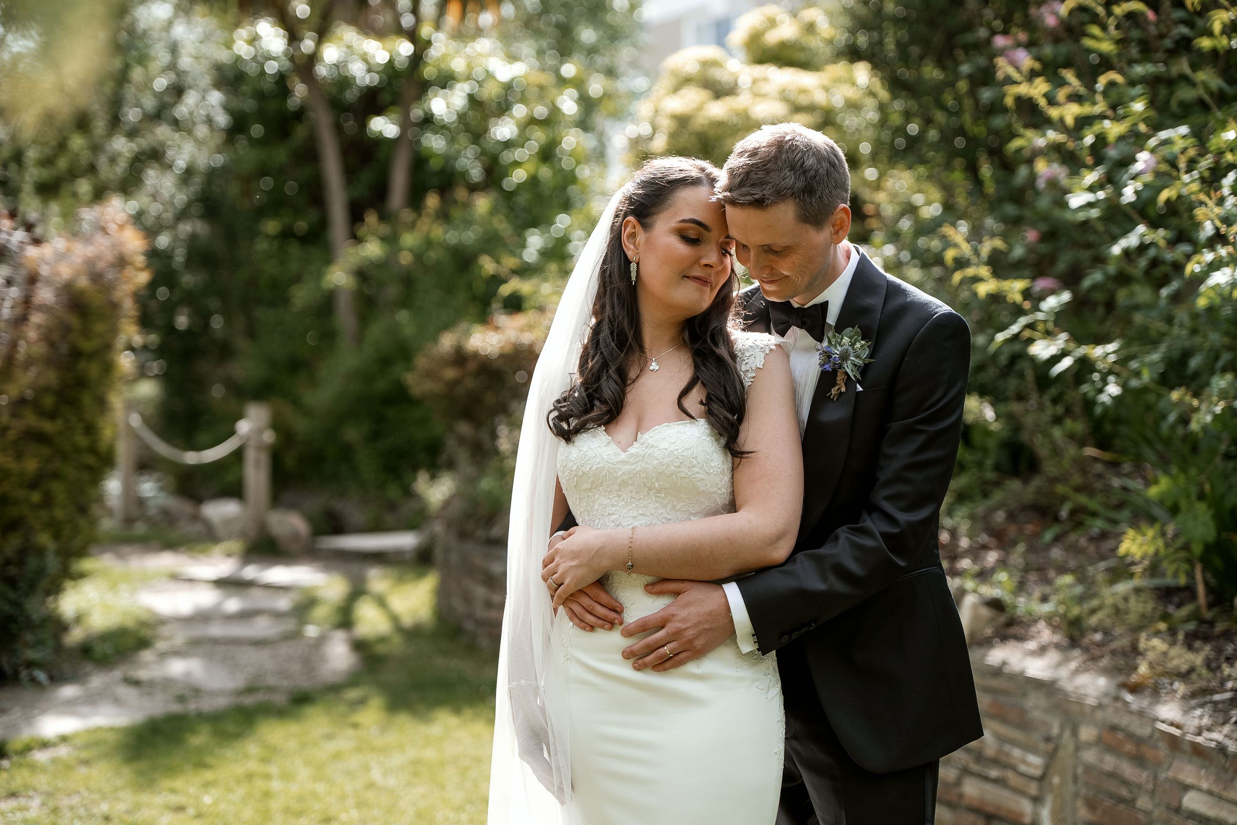 A romantic outdoor wedding portrait of a couple sharing an intimate moment in a sunlit garden setting.