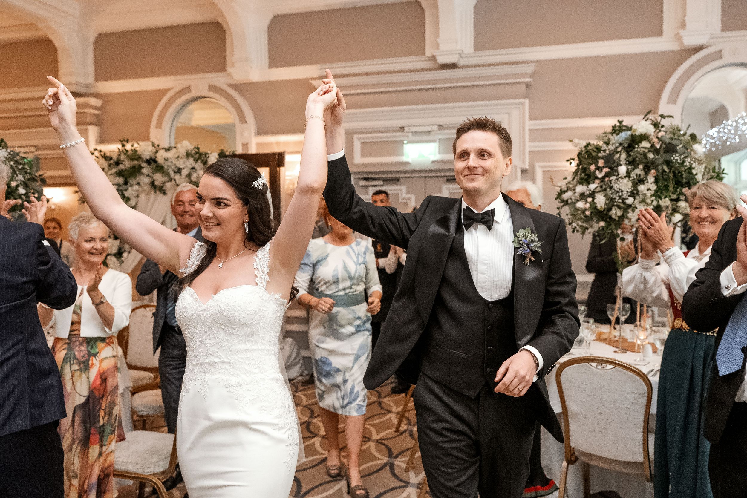 Newlywed couple celebrates with raised arms while walking down the aisle at an elegant indoor wedding reception.