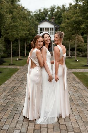 Bridesmaids in matching white dresses gather on stone patio during outdoor wedding.