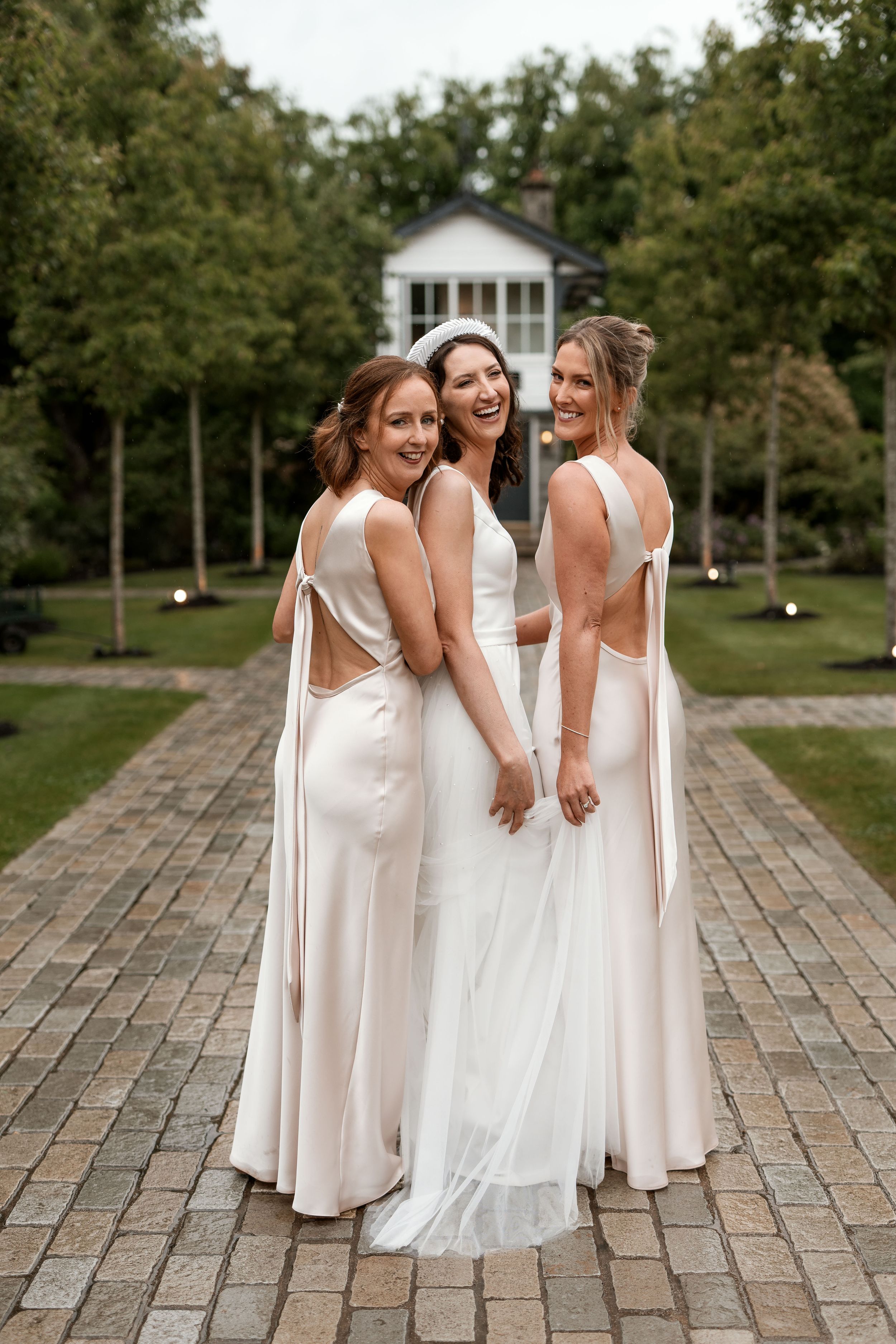 Bridesmaids in matching white dresses gather on stone patio during outdoor wedding.