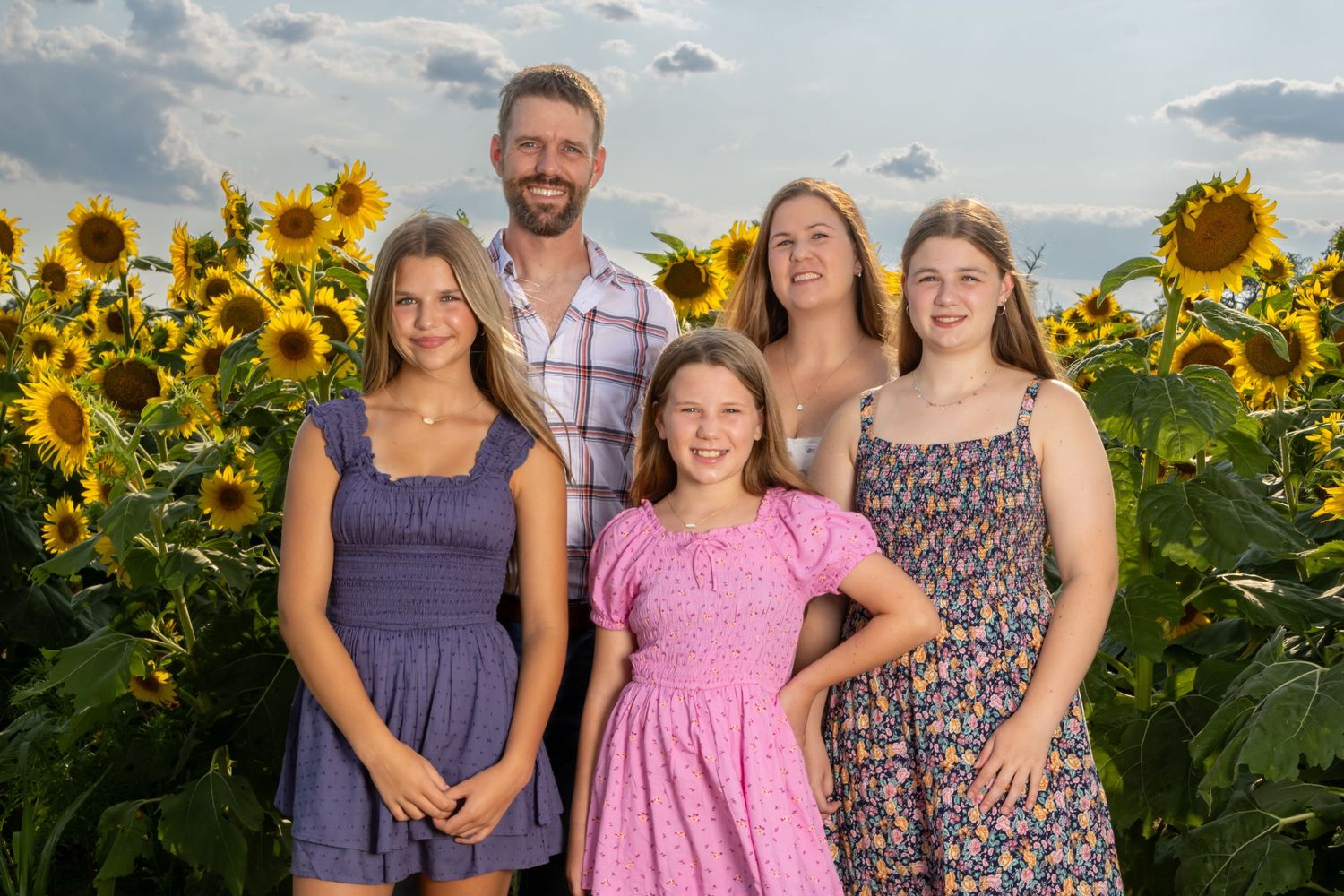 Family of five smiling in a sunflower field, with parents and three daughters. Salem and Gloucester County Family Photographer