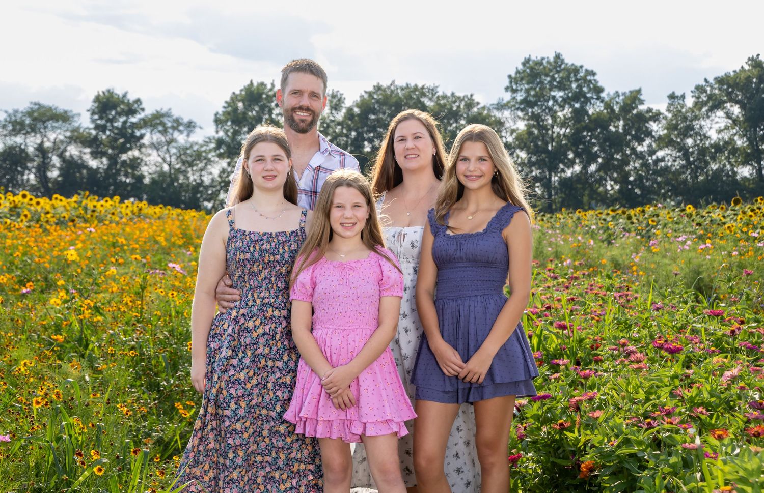 Family of five posing in a colorful wildflower meadow, with parents and three daughters smiling. Salem and Gloucester County Family Portrait