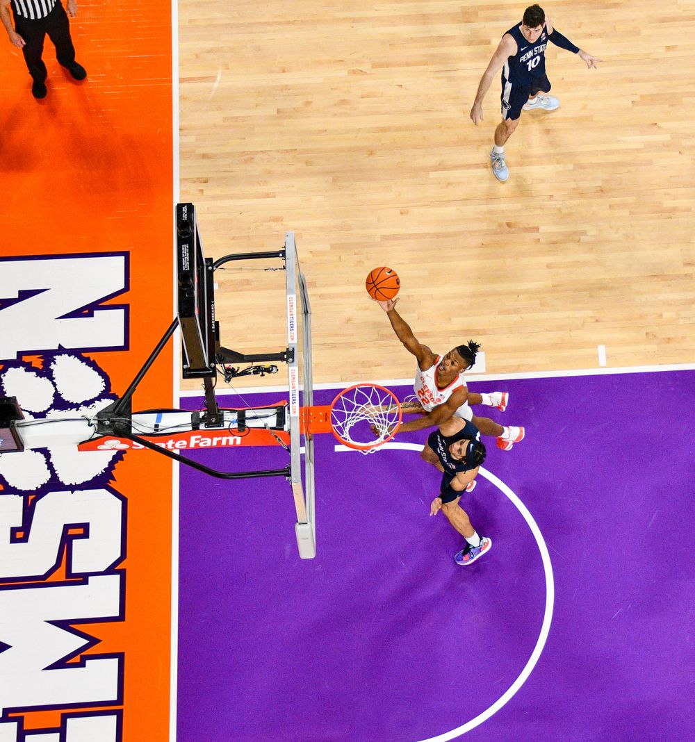 Basketball players compete for a shot near the hoop on purple and orange court.