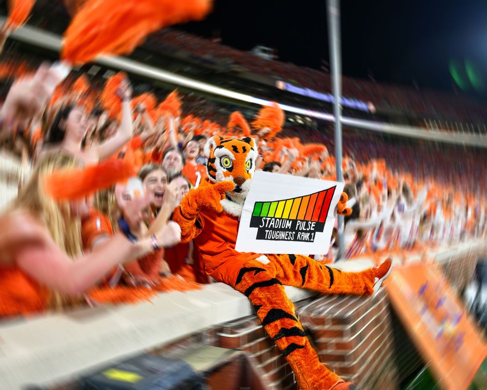 Mascot interacts with crowd while holding sign during energetic stadium moment.