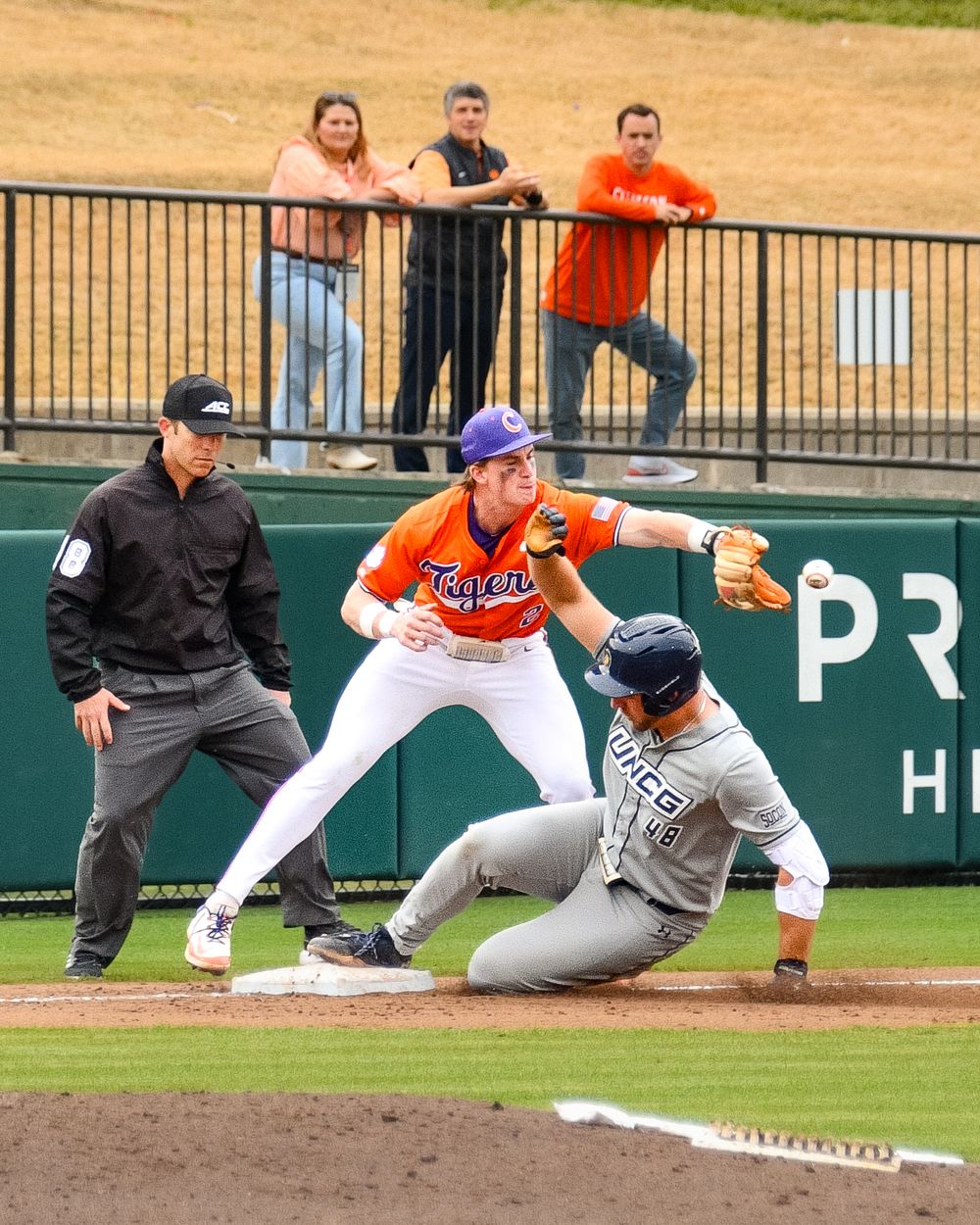 Baseball play at first base with fielder attempting to tag sliding runner while umpire watches.