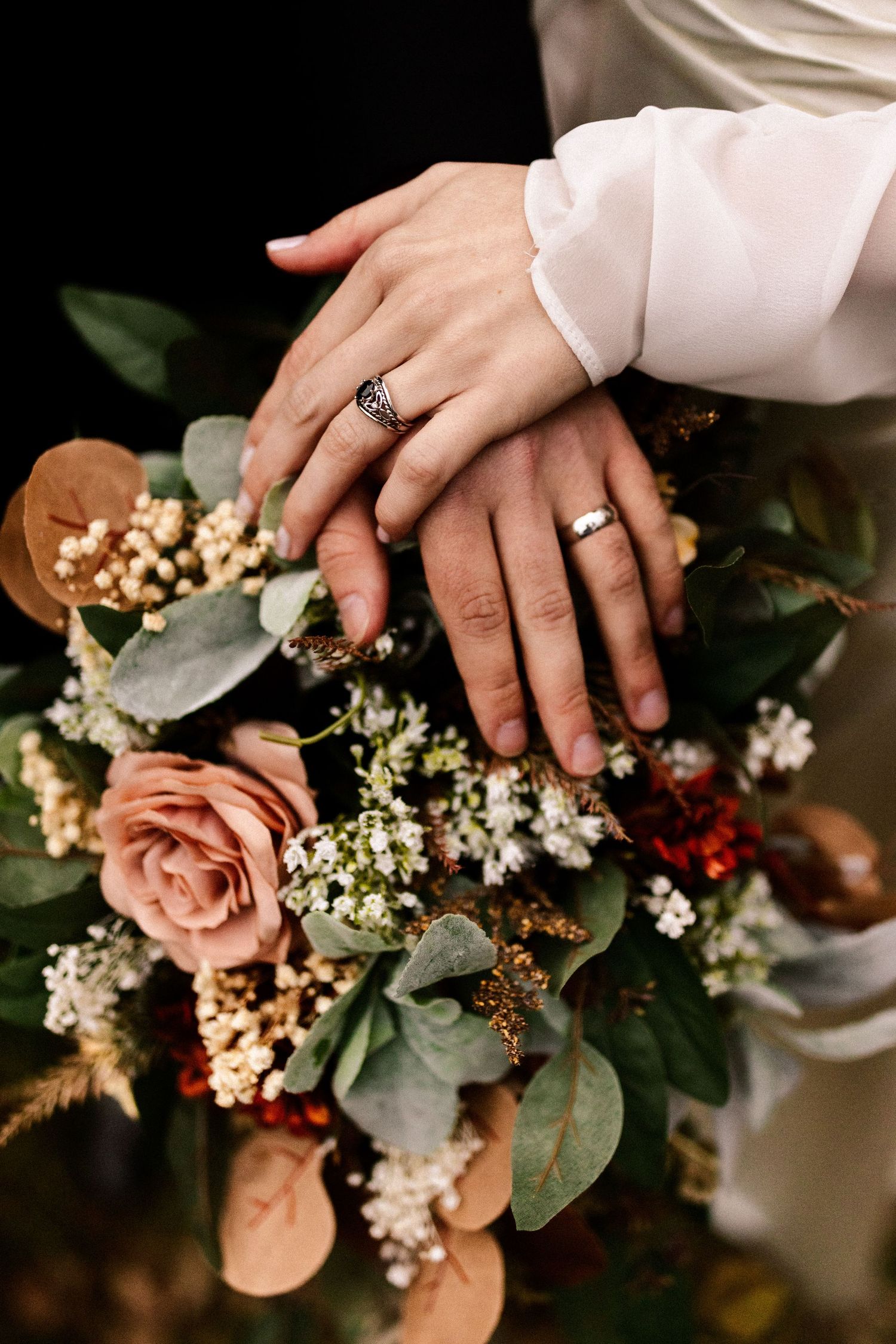 Close-up of wedding rings and delicate floral bouquet with eucalyptus and white blooms.