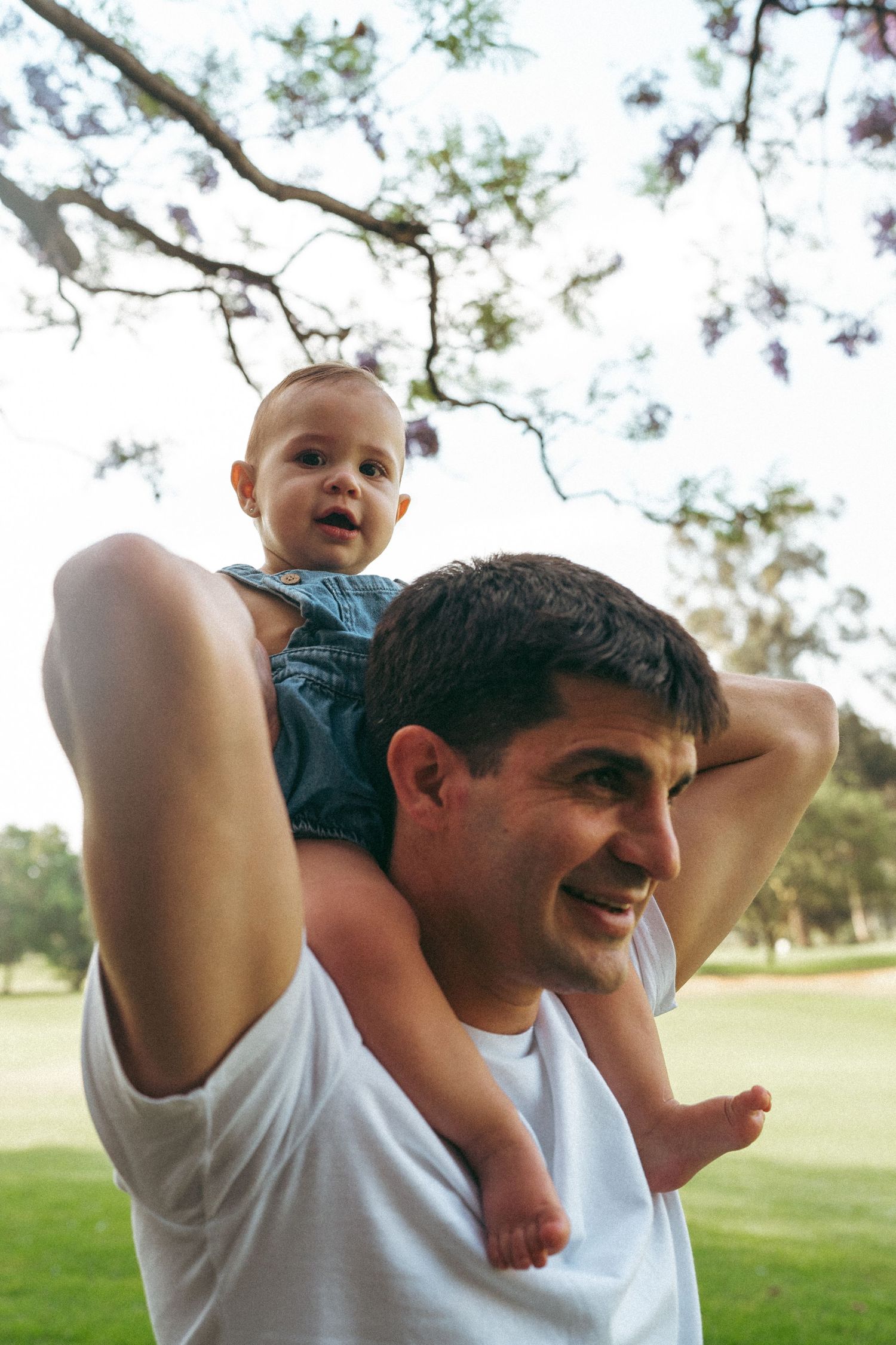 Parent lifting small child playfully under blooming spring trees.