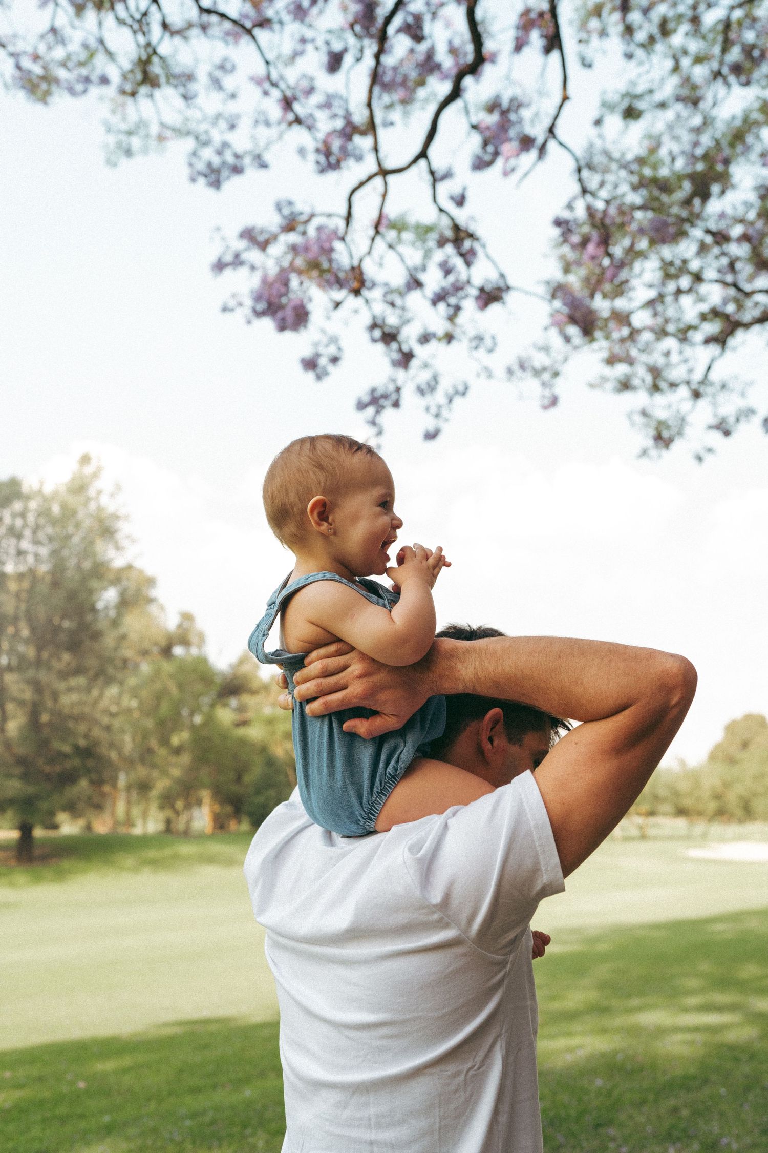 Parent and baby enjoying a sunny day under flowering trees in a park.