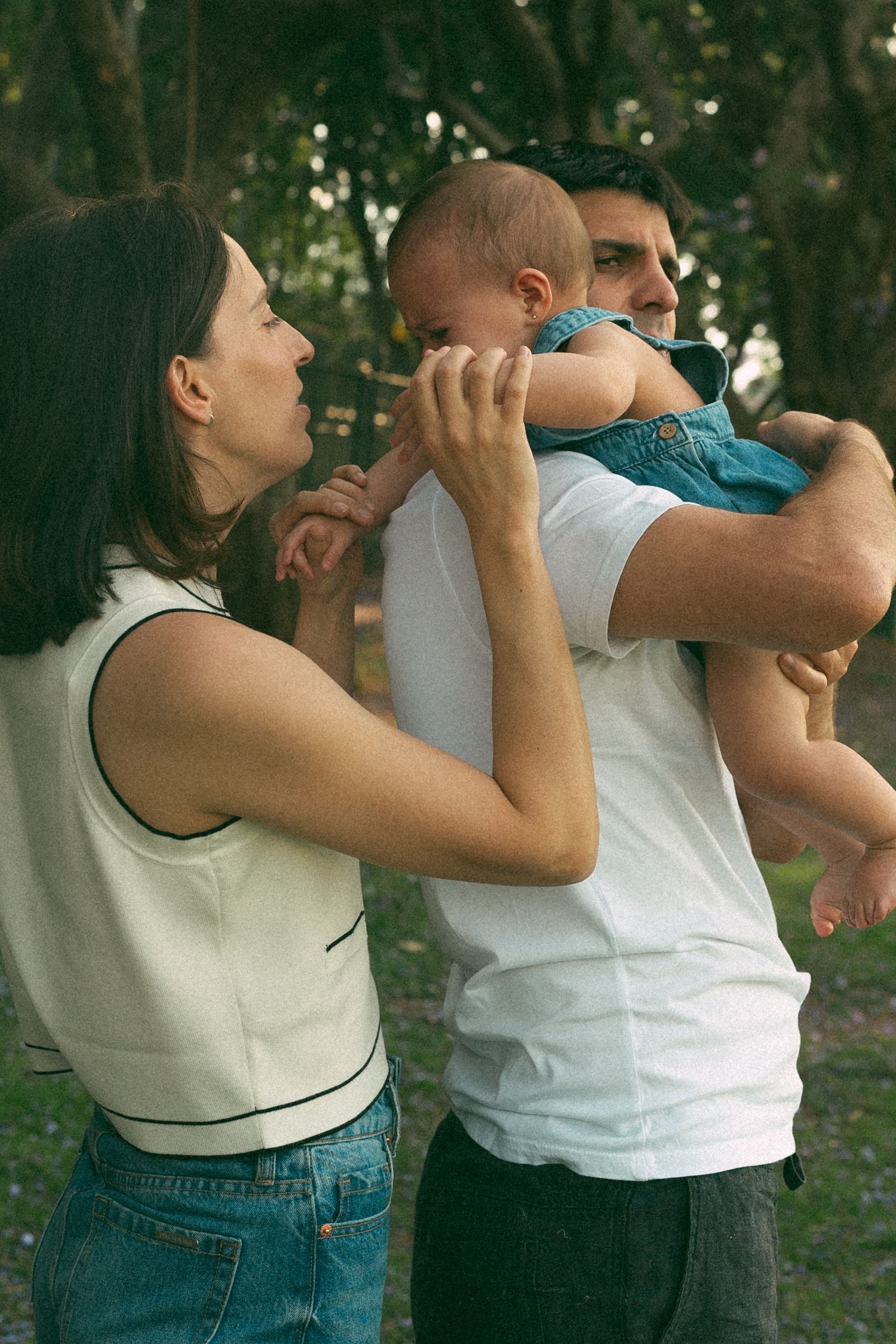 A tender family moment in a wooded setting as parents share affection with their baby.