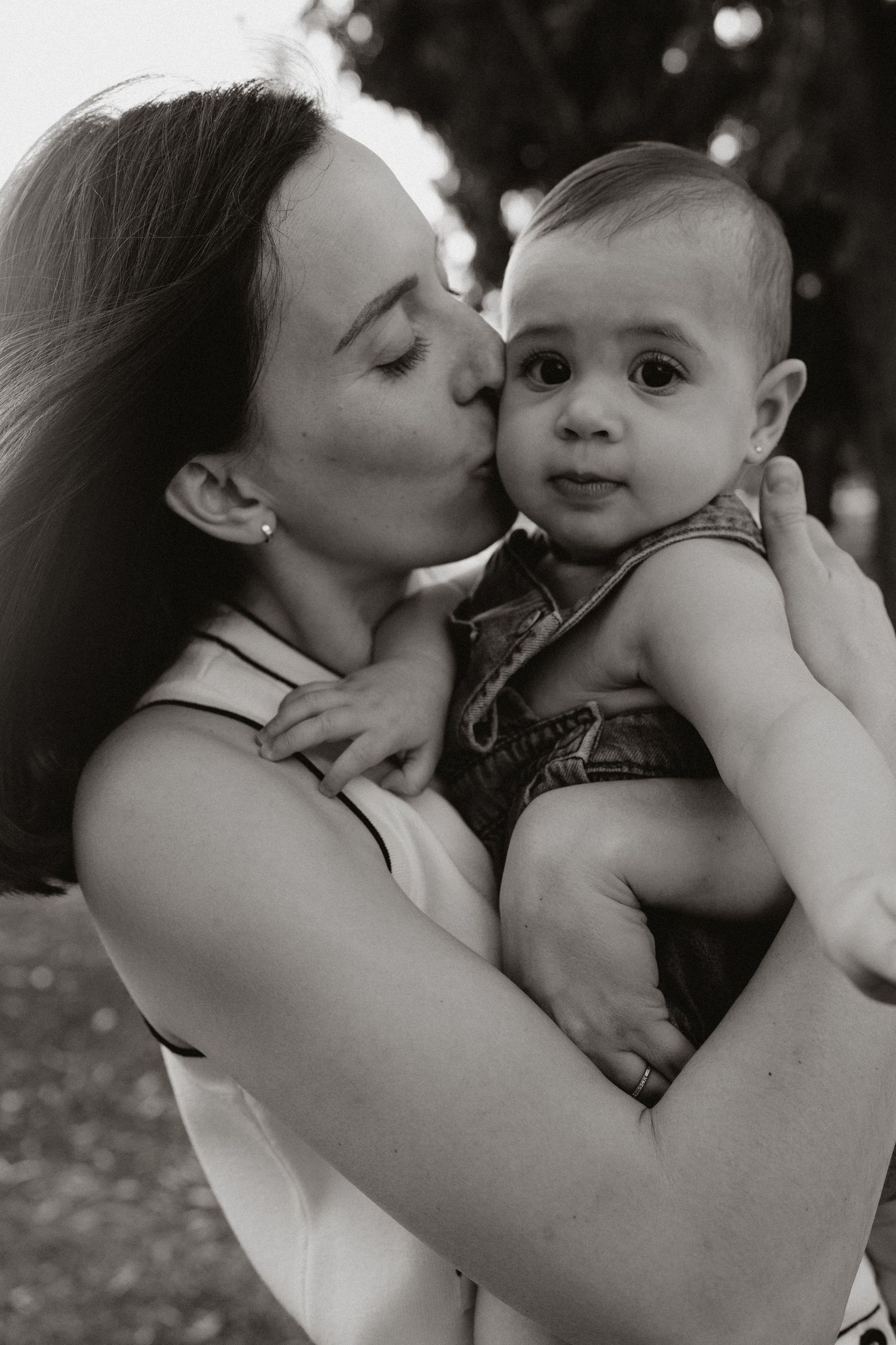 A sweet moment of affection between parent and baby outdoors in black and white.