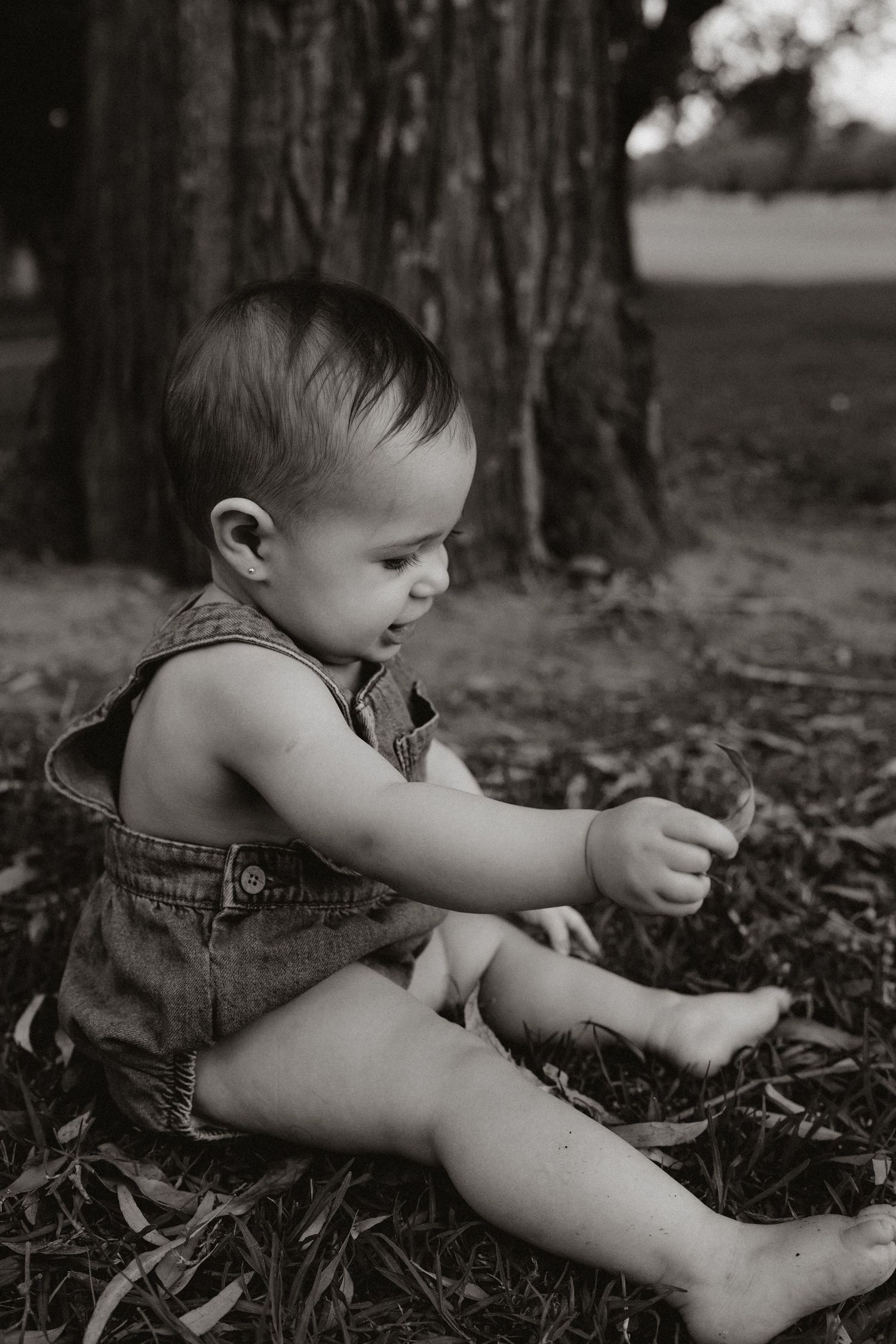 Black and white portrait of a baby exploring nature on the ground.