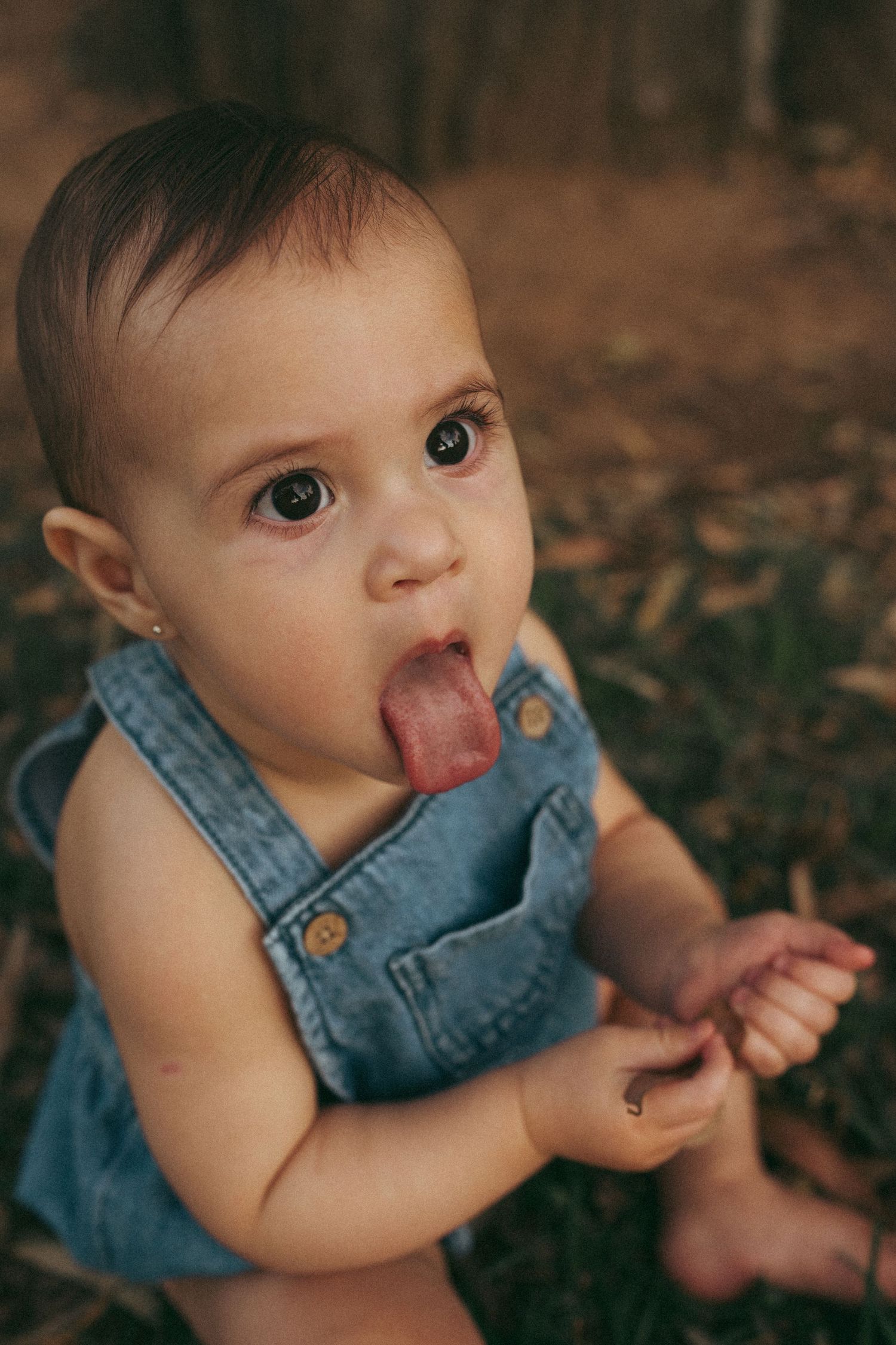 Close-up of a baby in denim overalls playing outdoors.