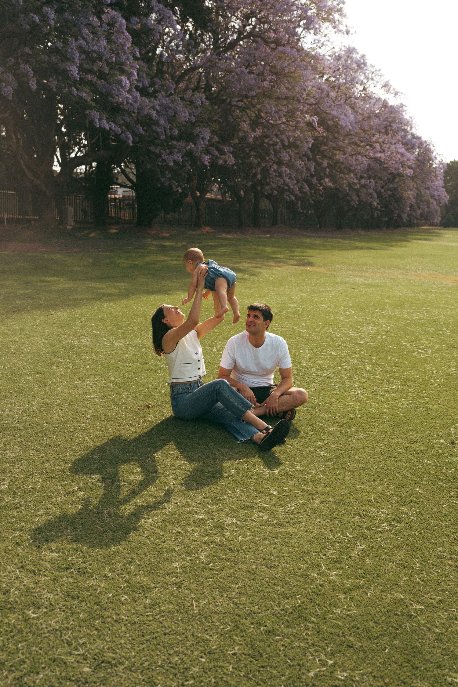 Two people lying on green grass having a playful moment under blooming trees.