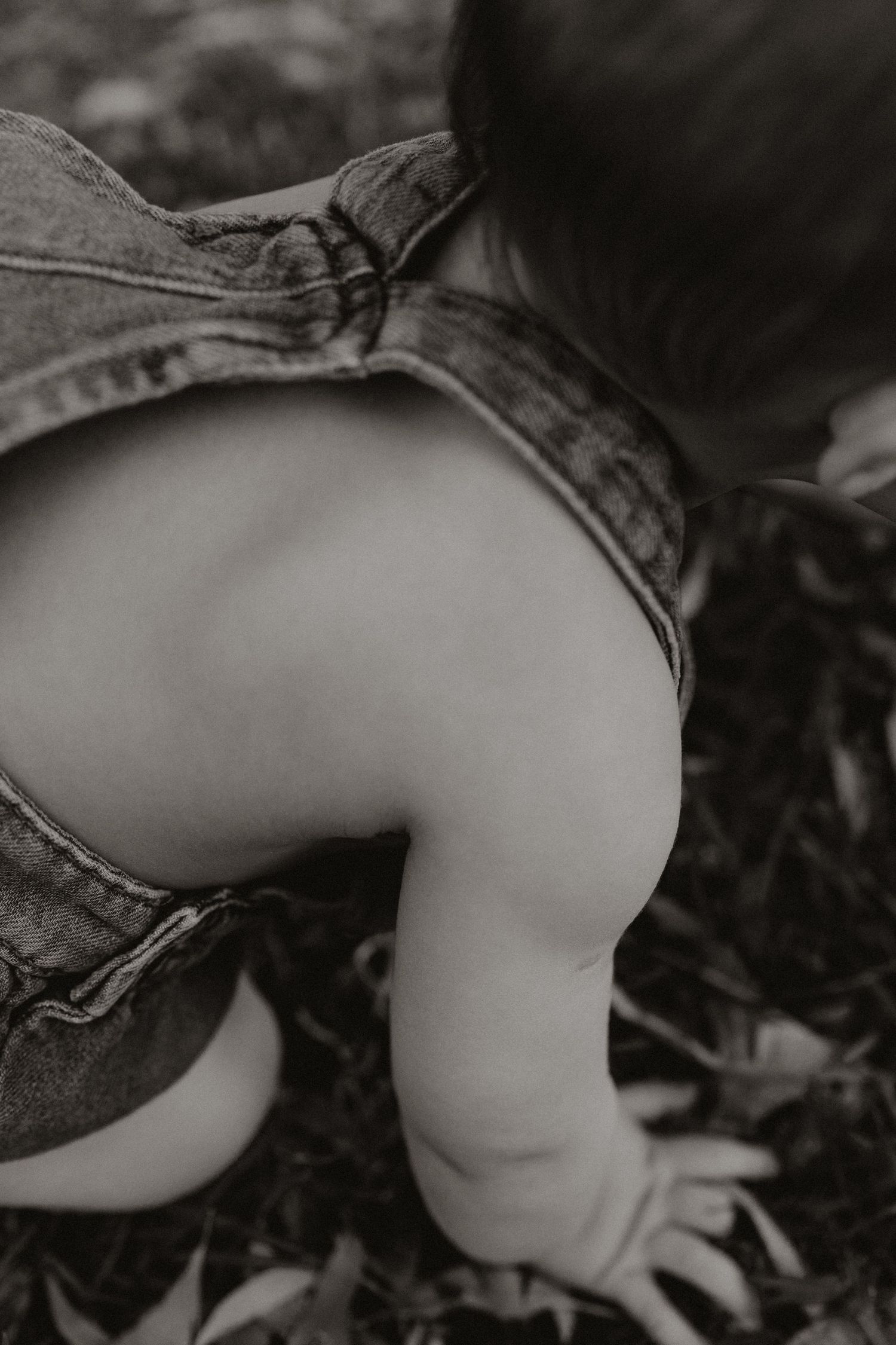 Close-up detail of baby's legs in denim against natural ground texture.