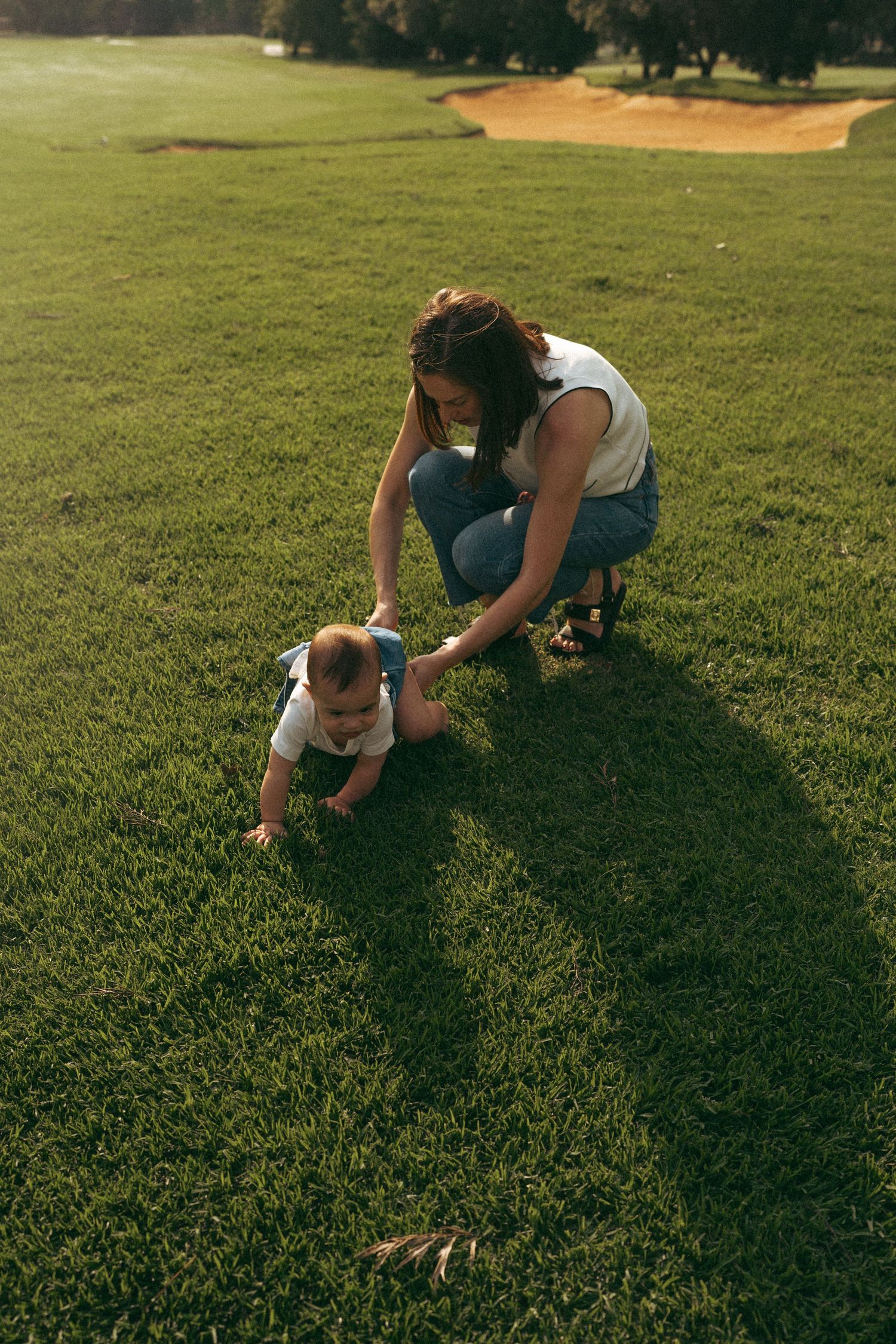 Person crawling on lush green grass in a park during golden hour.