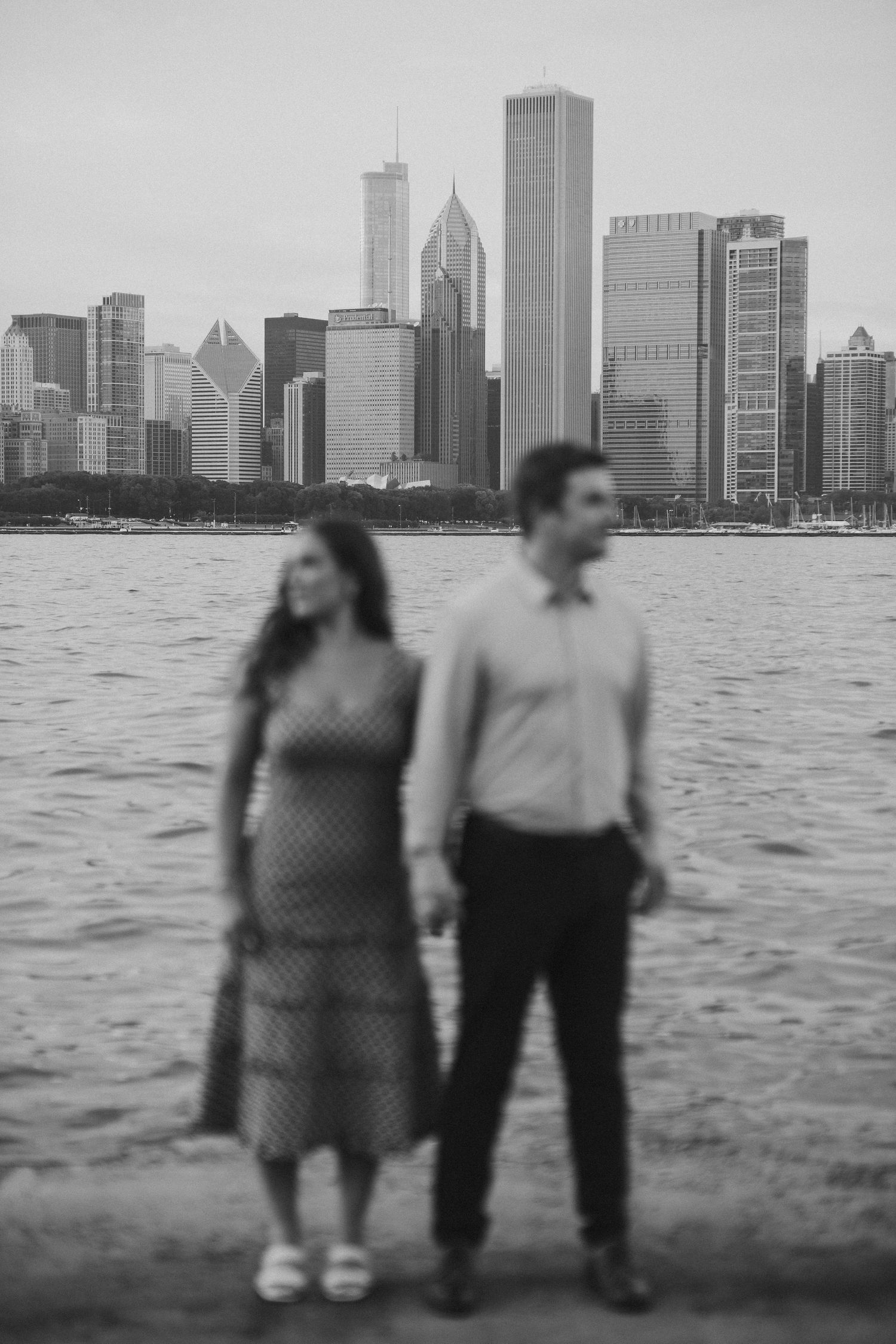 Black and white photo of couple standing by Chicago skyline and Lake Michigan.