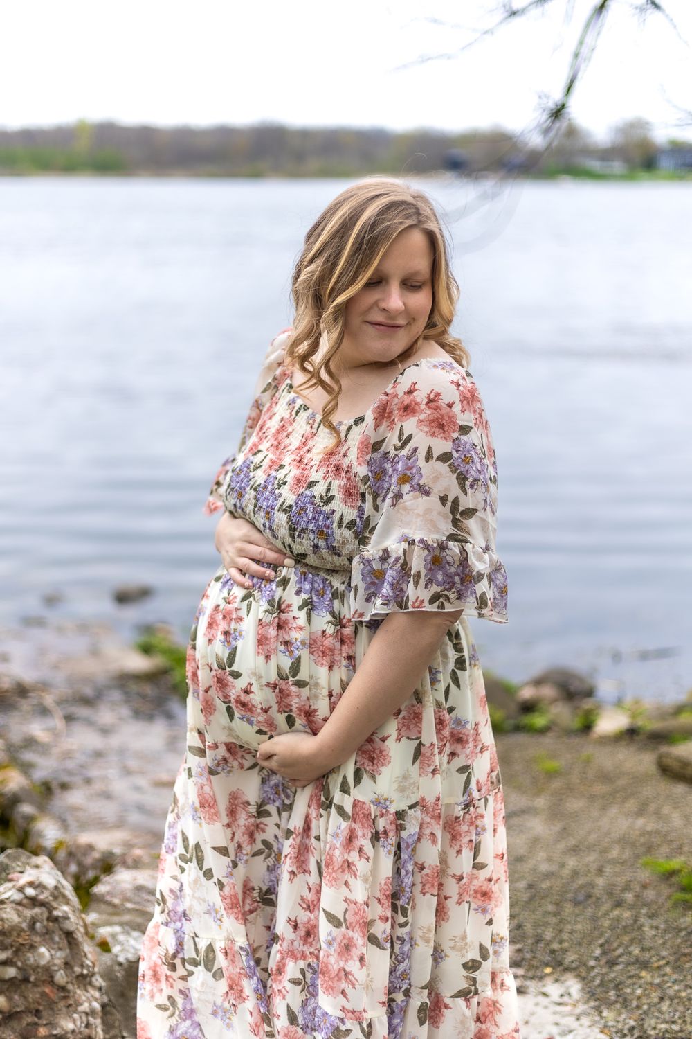 A maternity portrait by a lake featuring a floral dress against a peaceful waterfront backdrop.
