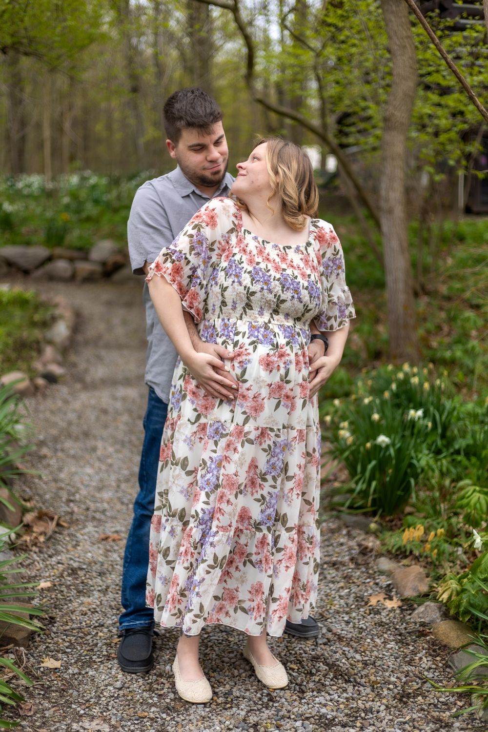A tender maternity moment captured on a garden path surrounded by spring greenery.