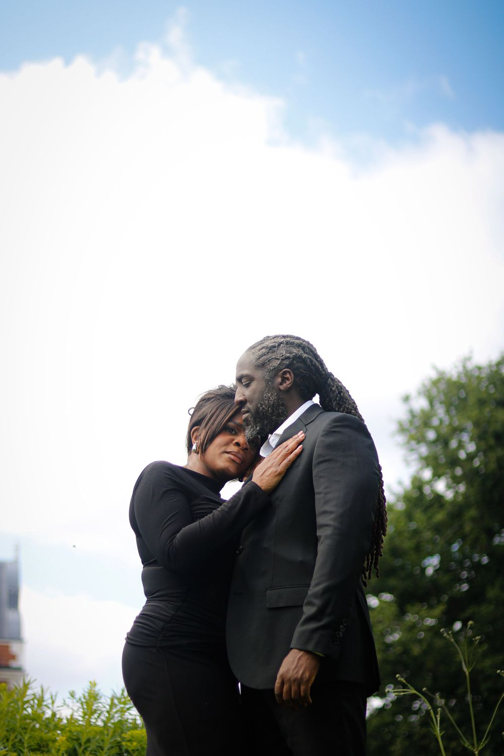 A couple shares an intimate moment against a bright blue sky with clouds.