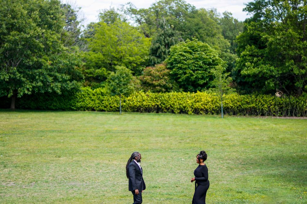 Two people stand in conversation on a lush green lawn surrounded by trees.