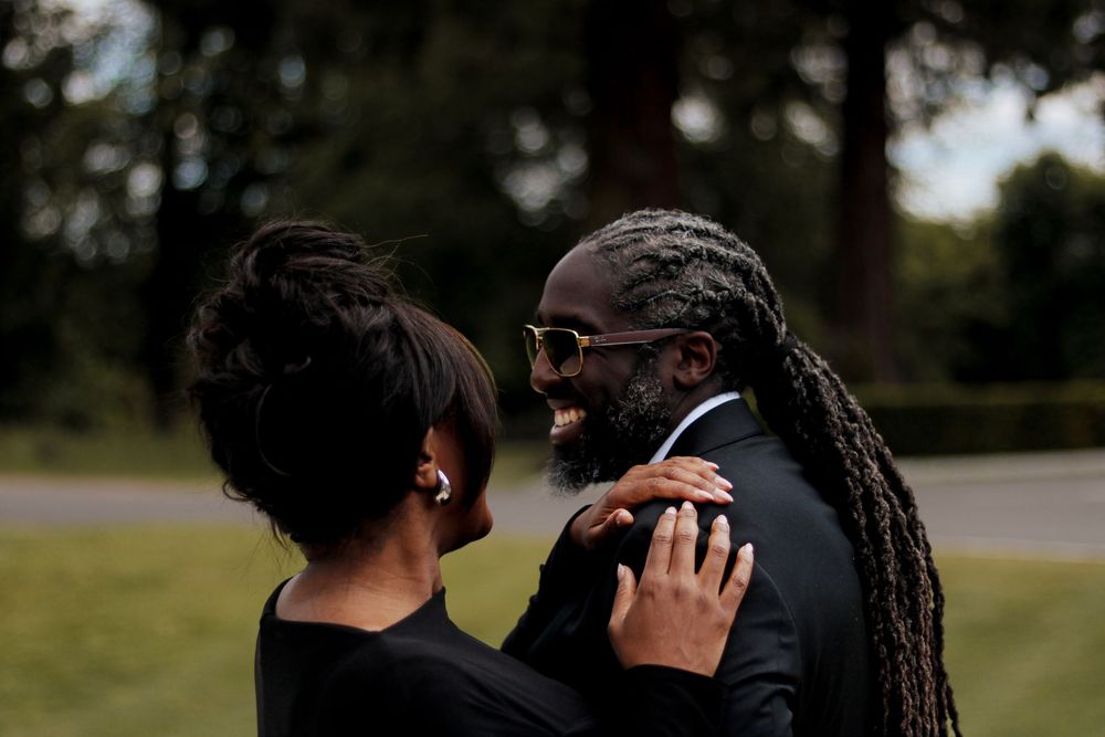 A couple shares a tender moment outdoors in formal black attire.