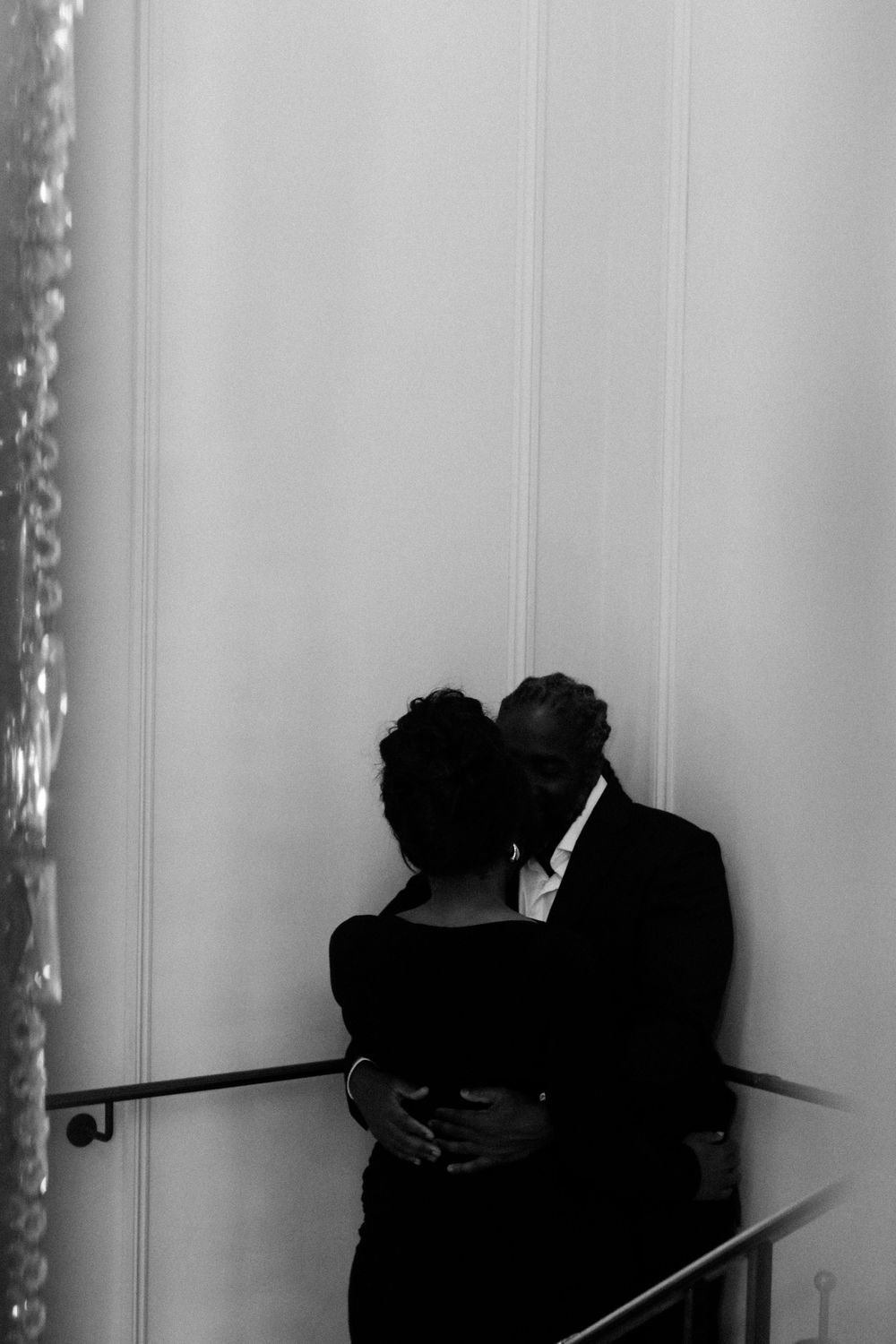 Silhouetted figures embracing against white wall with dramatic lighting.