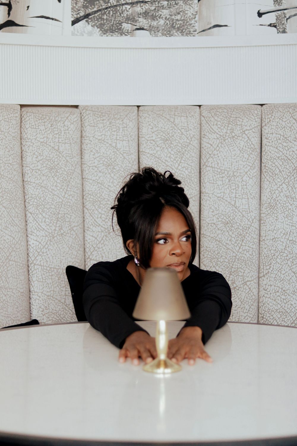 A creative portrait shot of someone leaning over a table with a gold lamp.