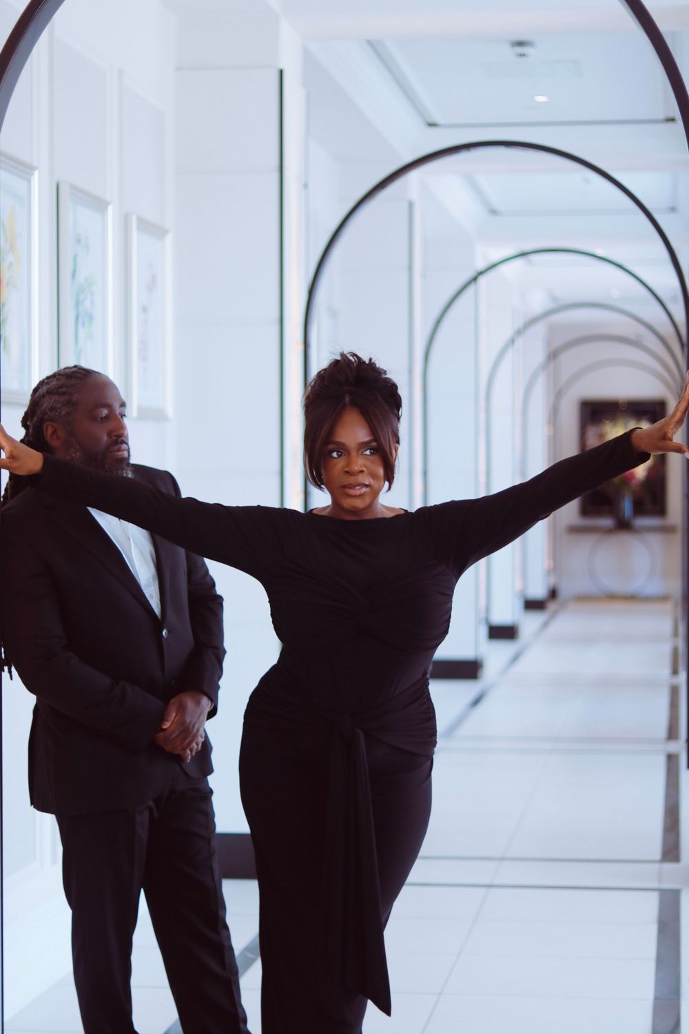 Couple in black formal wear dancing and posing in white arched hallway.