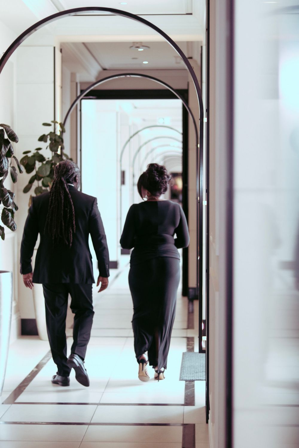 People walking through elegant white hallway with arched doorways.