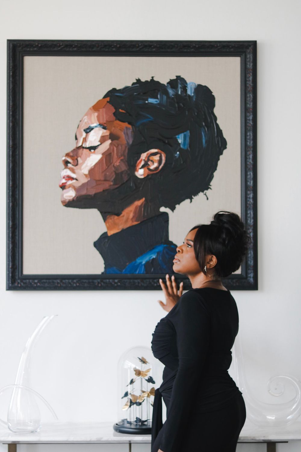 A person stands beside a striking portrait painting in a black frame.