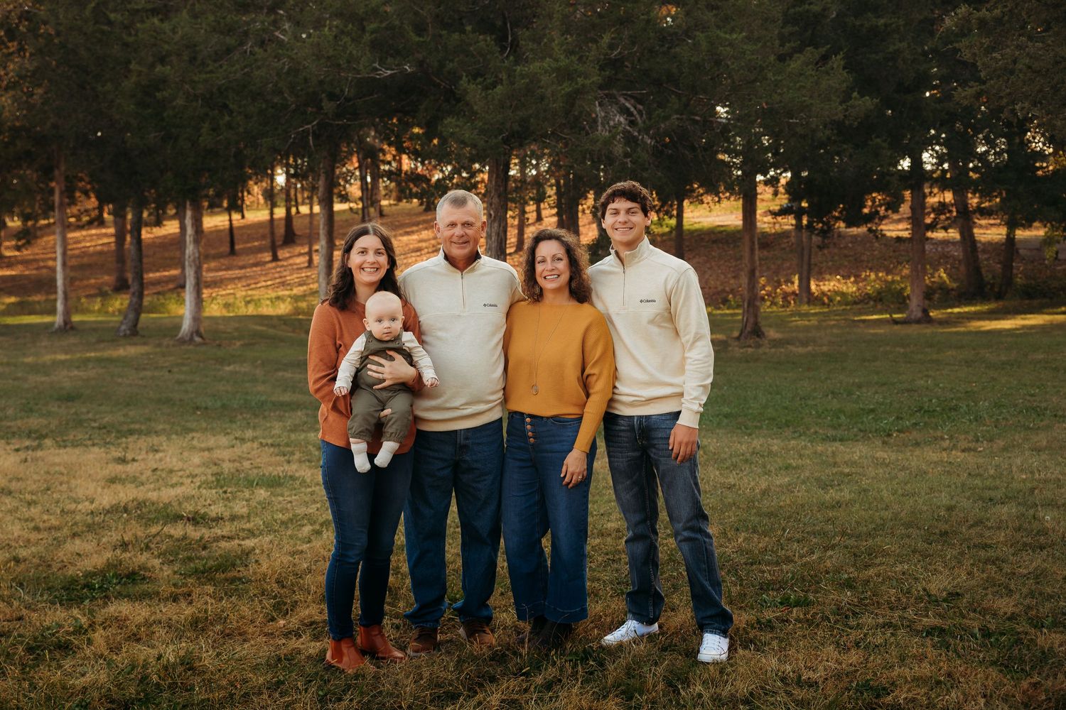 Family group wearing coordinated outfits poses together in autumn park setting.