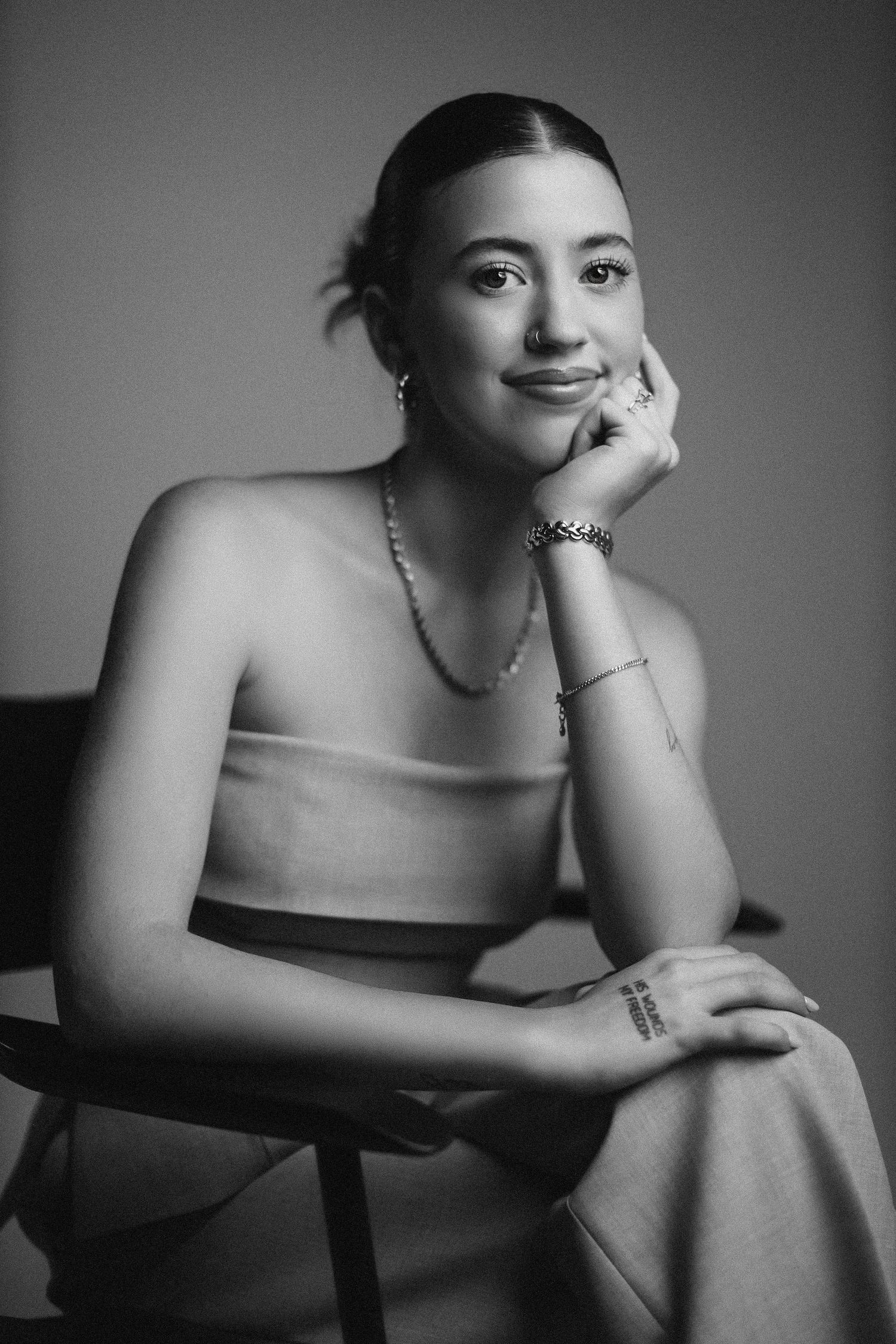 Black and white portrait of young woman in elegant attire resting chin on hand while seated.