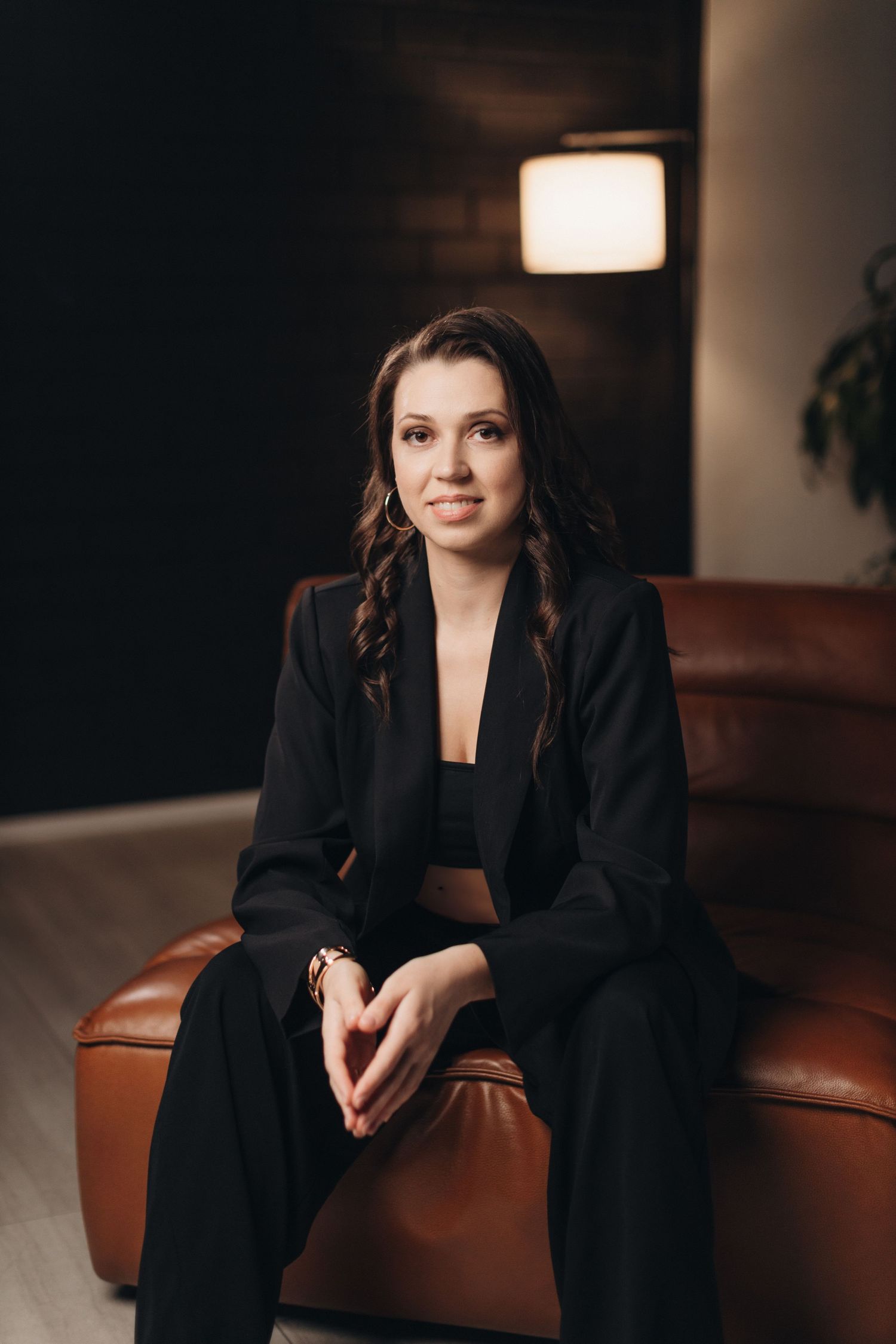 Studio portrait of a person in black business attire seated on a leather couch.