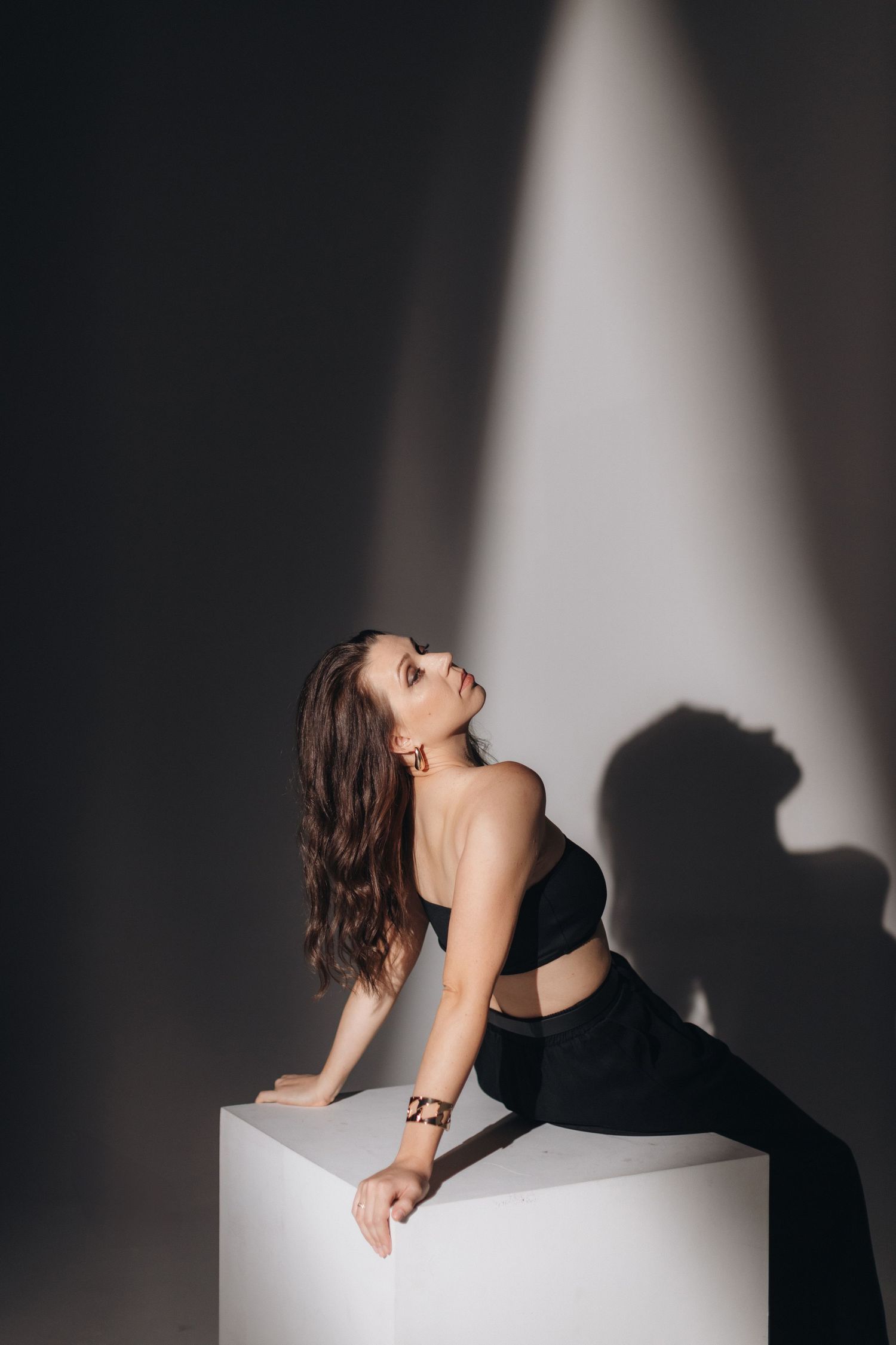 Artistic photo of a dancer in black attire posing on a white cube with dramatic lighting.