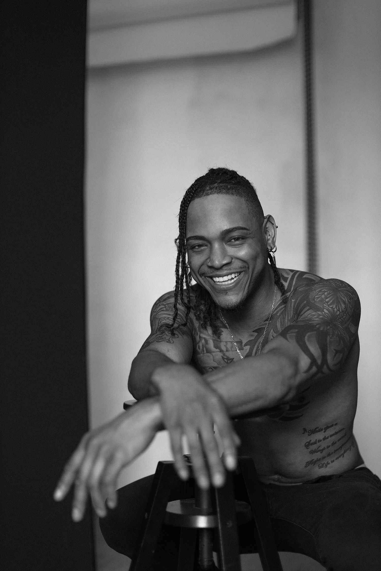 Black and white portrait showing tattooed person smiling warmly at camera.