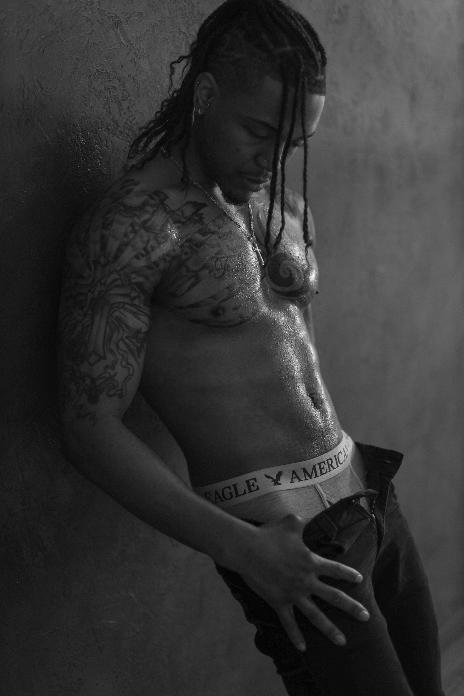 Artistic black and white photo showing tattooed torso against textured wall.