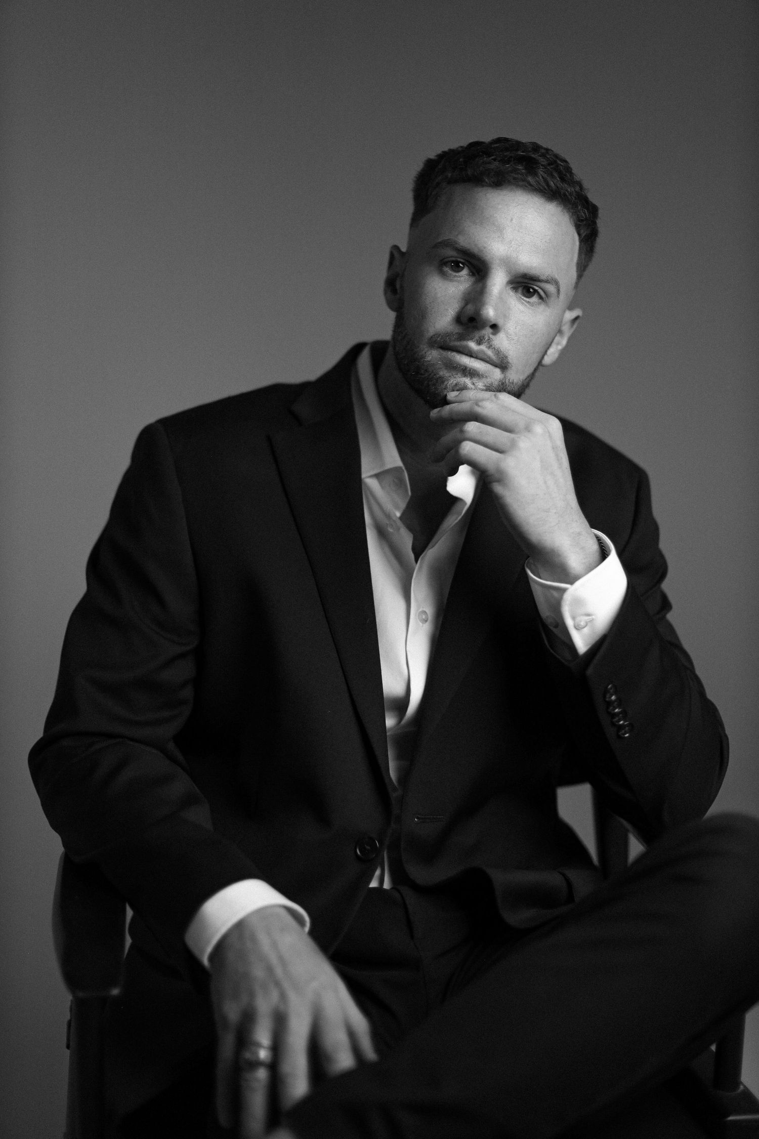 Black and white portrait of man in suit posing thoughtfully in studio setting.