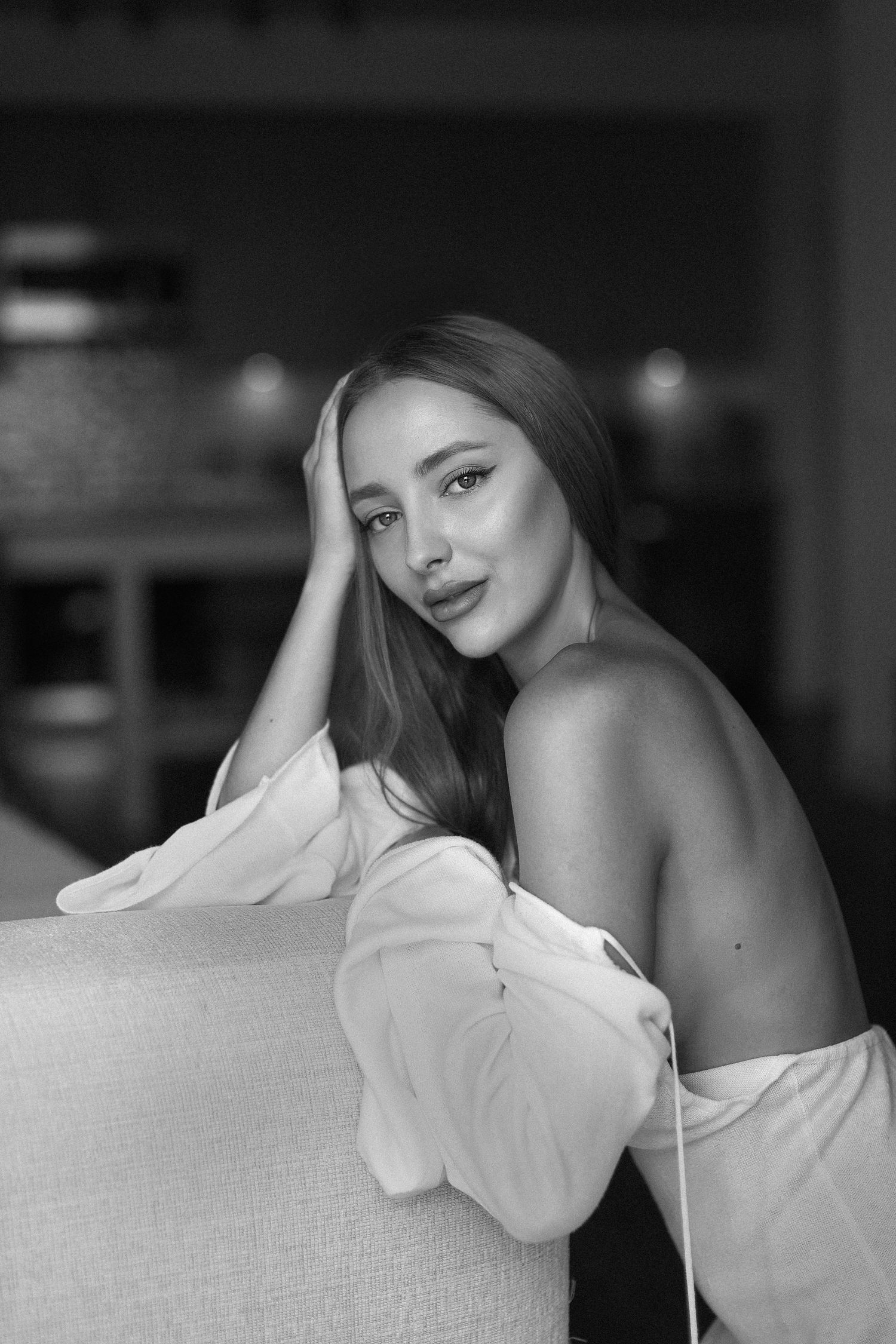 Artistic black and white portrait of a model posing on a couch in intimate attire.