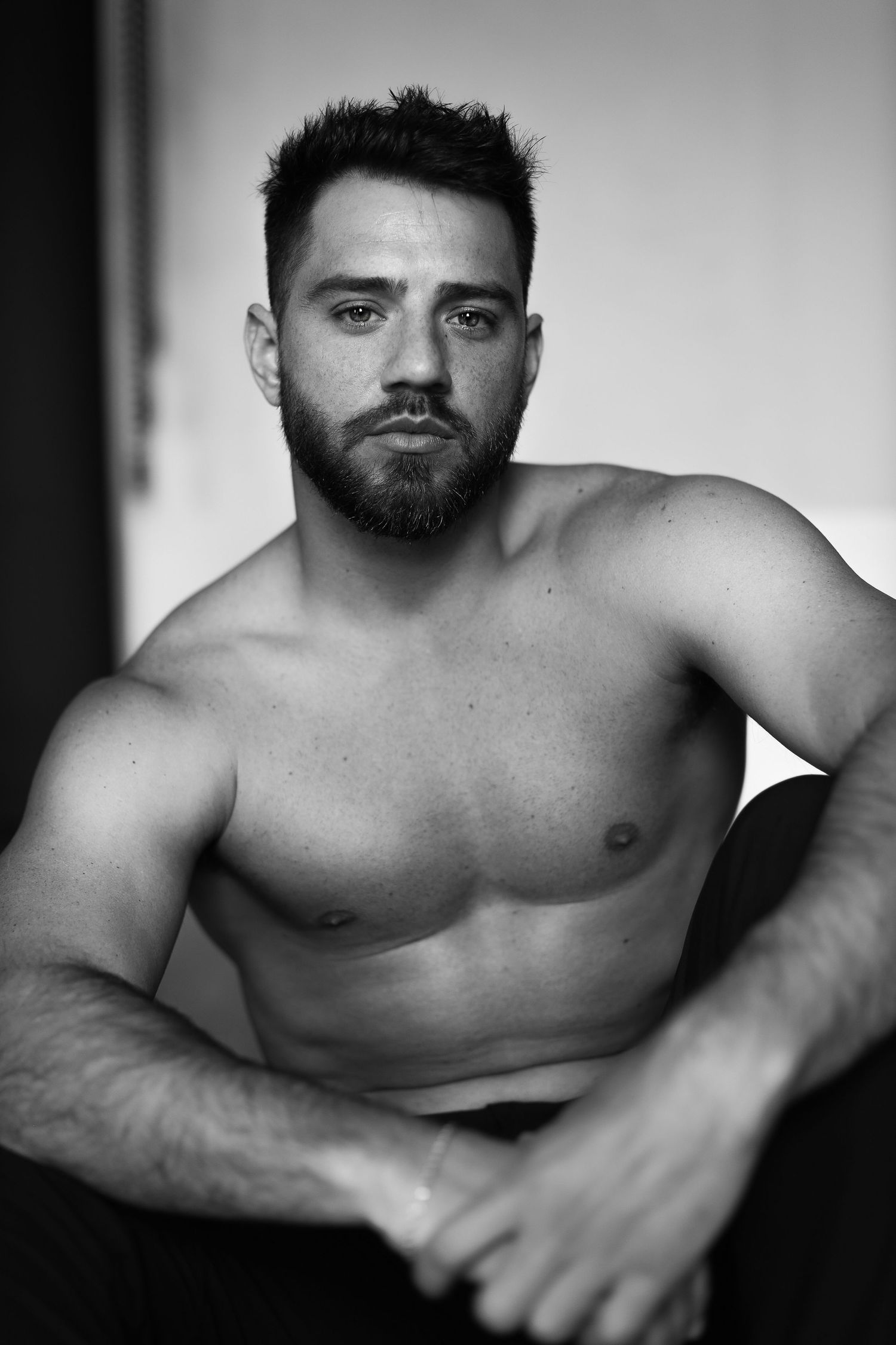 Black and white studio portrait of a muscular bearded man in dramatic lighting.