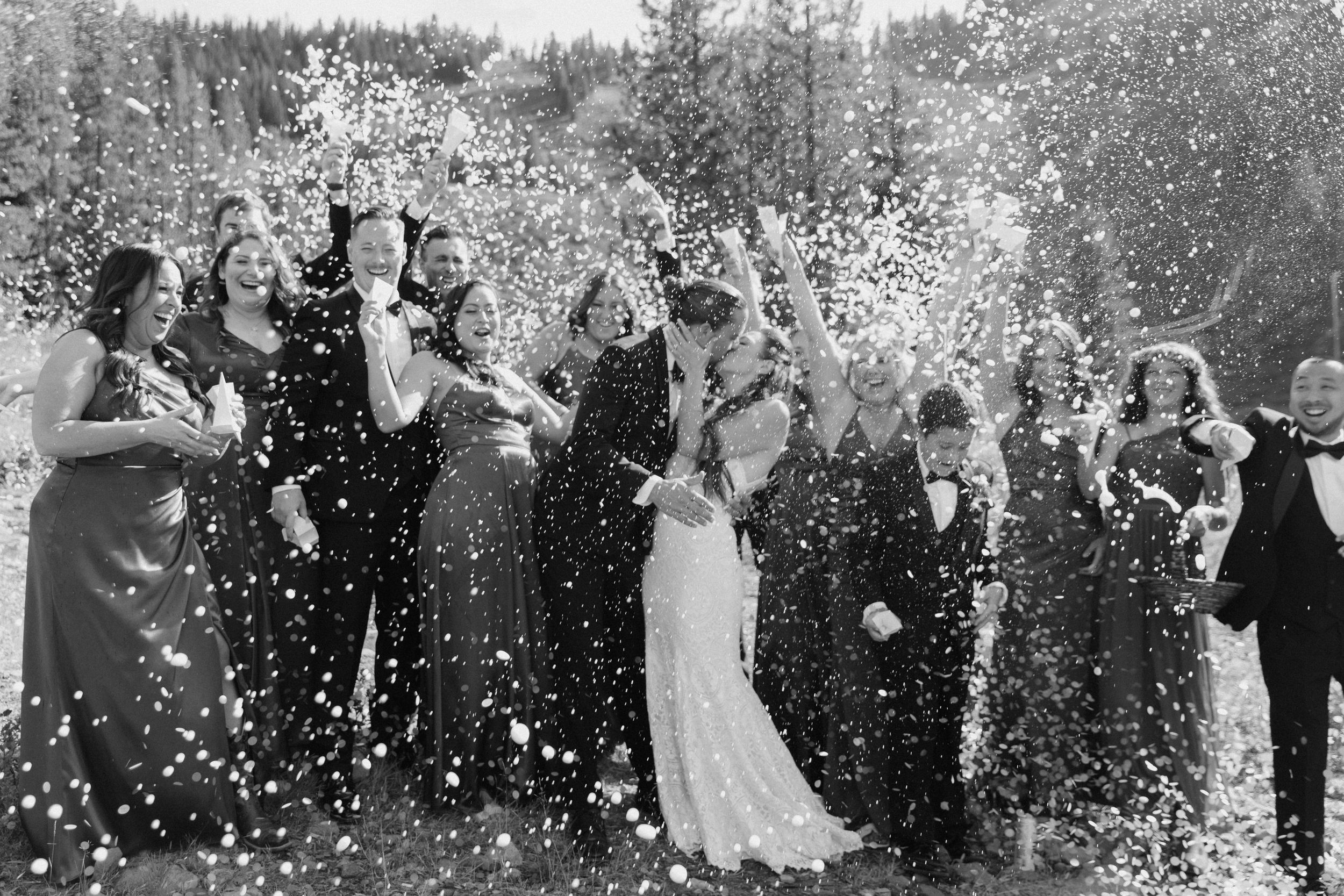 bridal party popping bottles of champagne while the bride and groom share a kiss