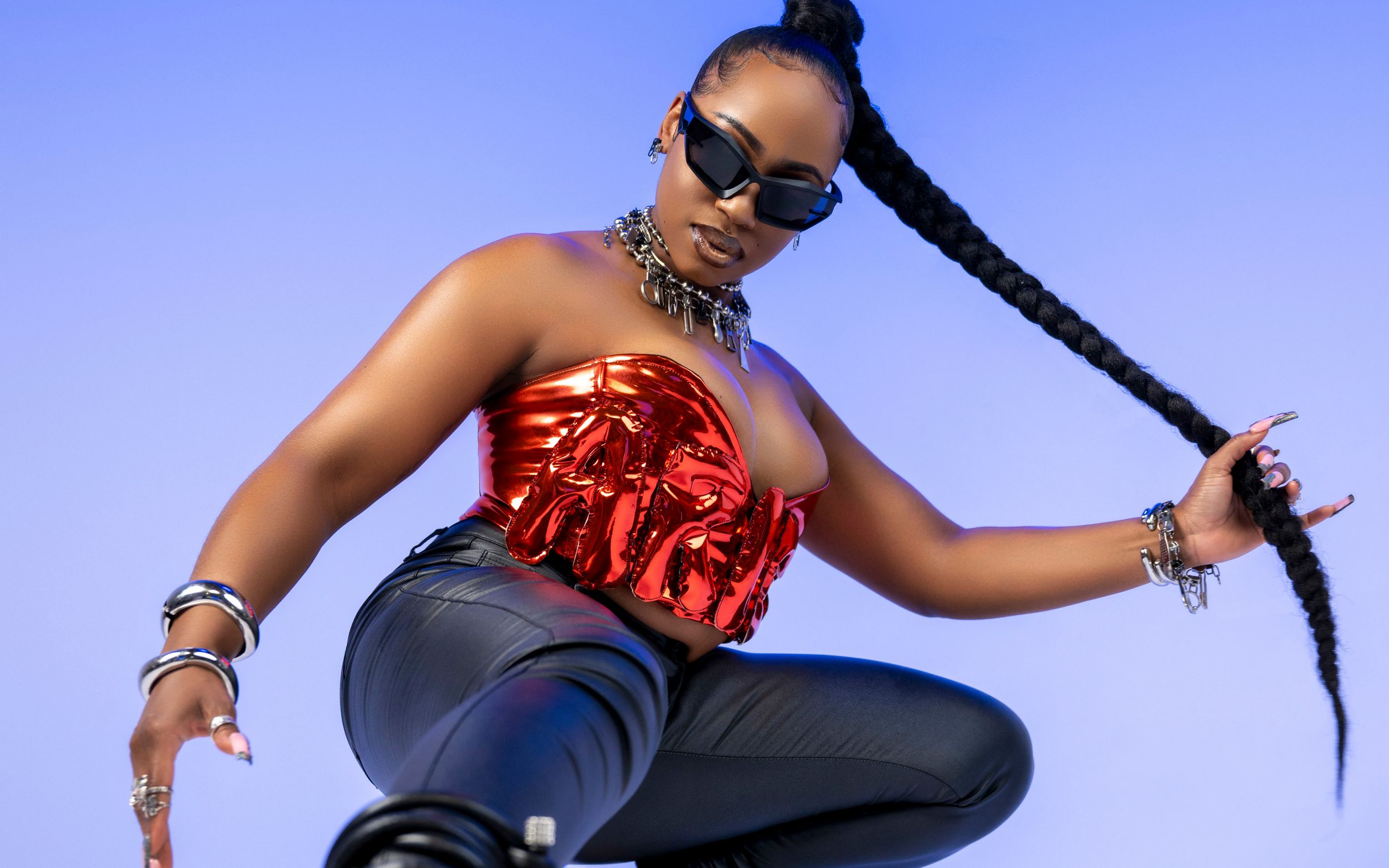 Performer in red metallic top and black pants strikes dynamic pose with long braided hair.