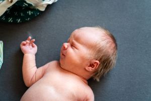 A newborn baby sleeps peacefully on a dark background showing delicate features.