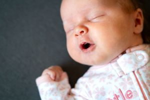A sleeping newborn baby wearing pink floral clothing rests against a dark background.
