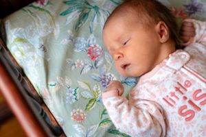 A peaceful sleeping infant rests on floral bedding wearing soft pink clothing.