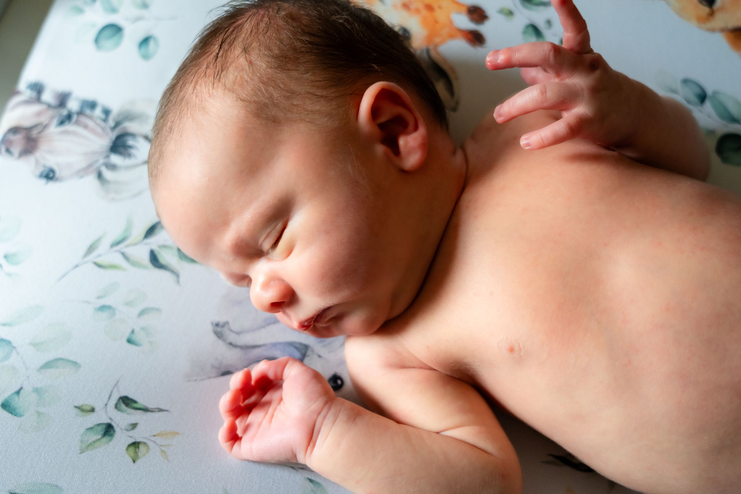 Sleeping newborn on floral patterned fabric in natural lighting.