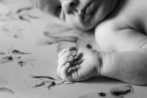 Black and white close-up of tiny newborn hand resting on floral textured fabric.
