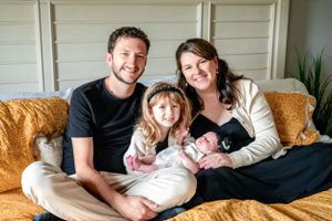 Happy family of four relaxing together on yellow couch at home.