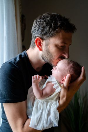 A tender moment between a parent in black shirt gently kissing a newborn baby wearing white.