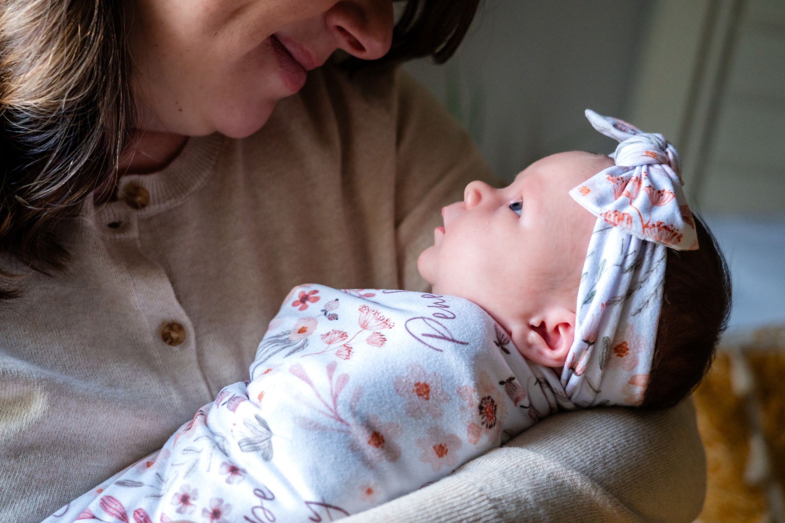 A parent gazes lovingly at a sleeping newborn wearing a floral outfit and bow.